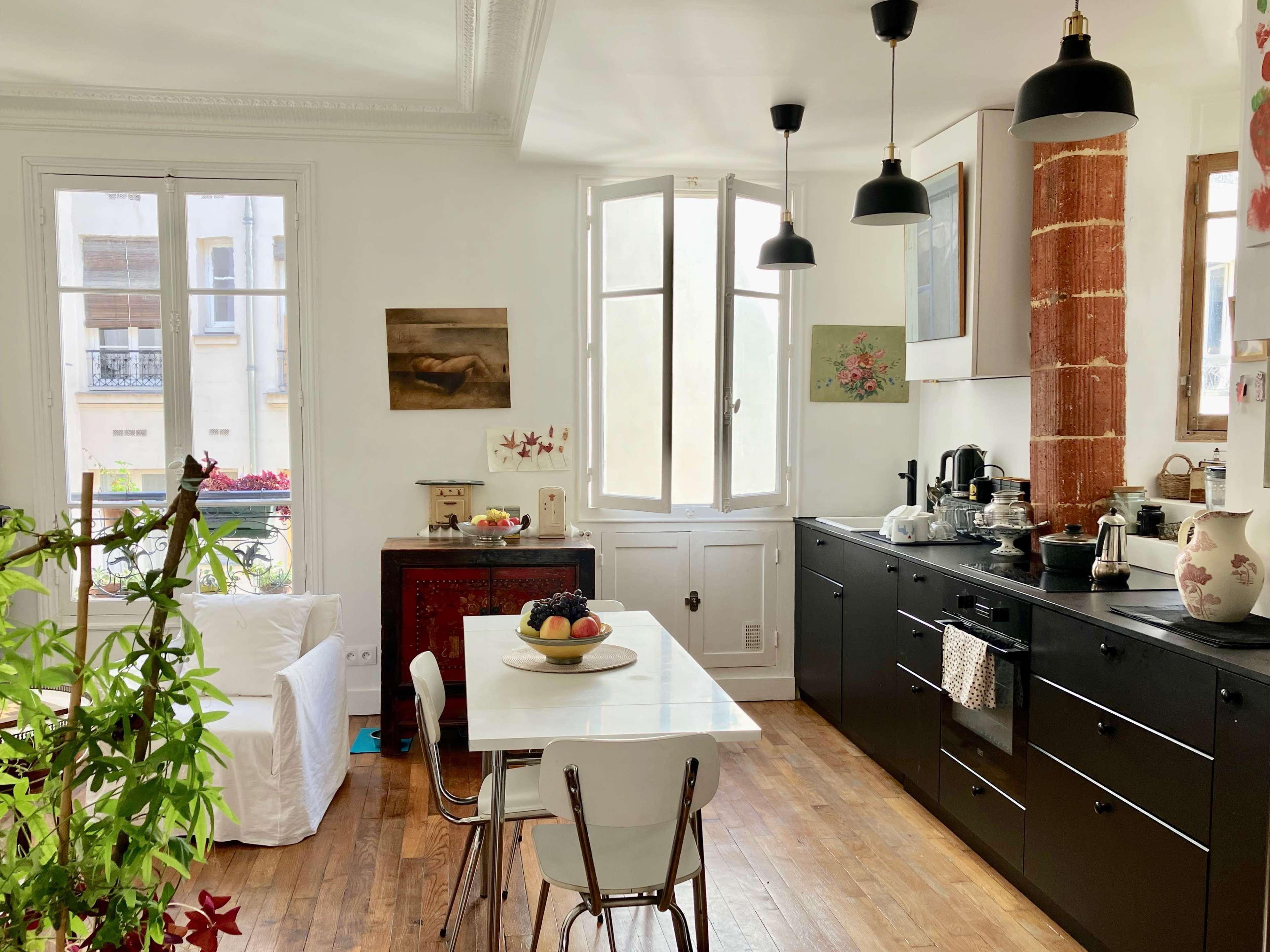 A modern kitchen features black cabinetry, a white dining table with chairs, and large windows illuminating the space.