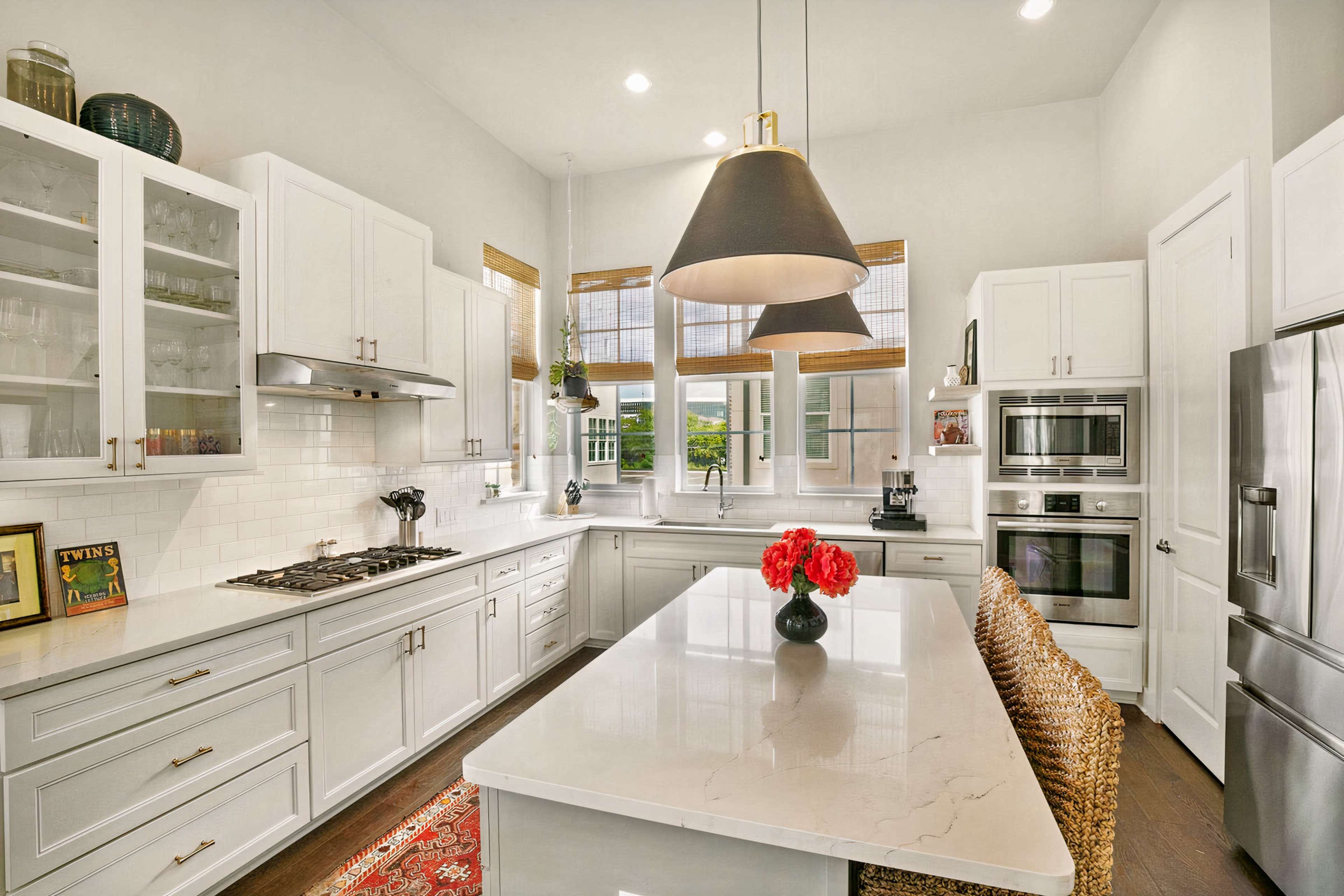 A modern kitchen features white cabinetry, stainless steel appliances, and a large island with a flower arrangement.
