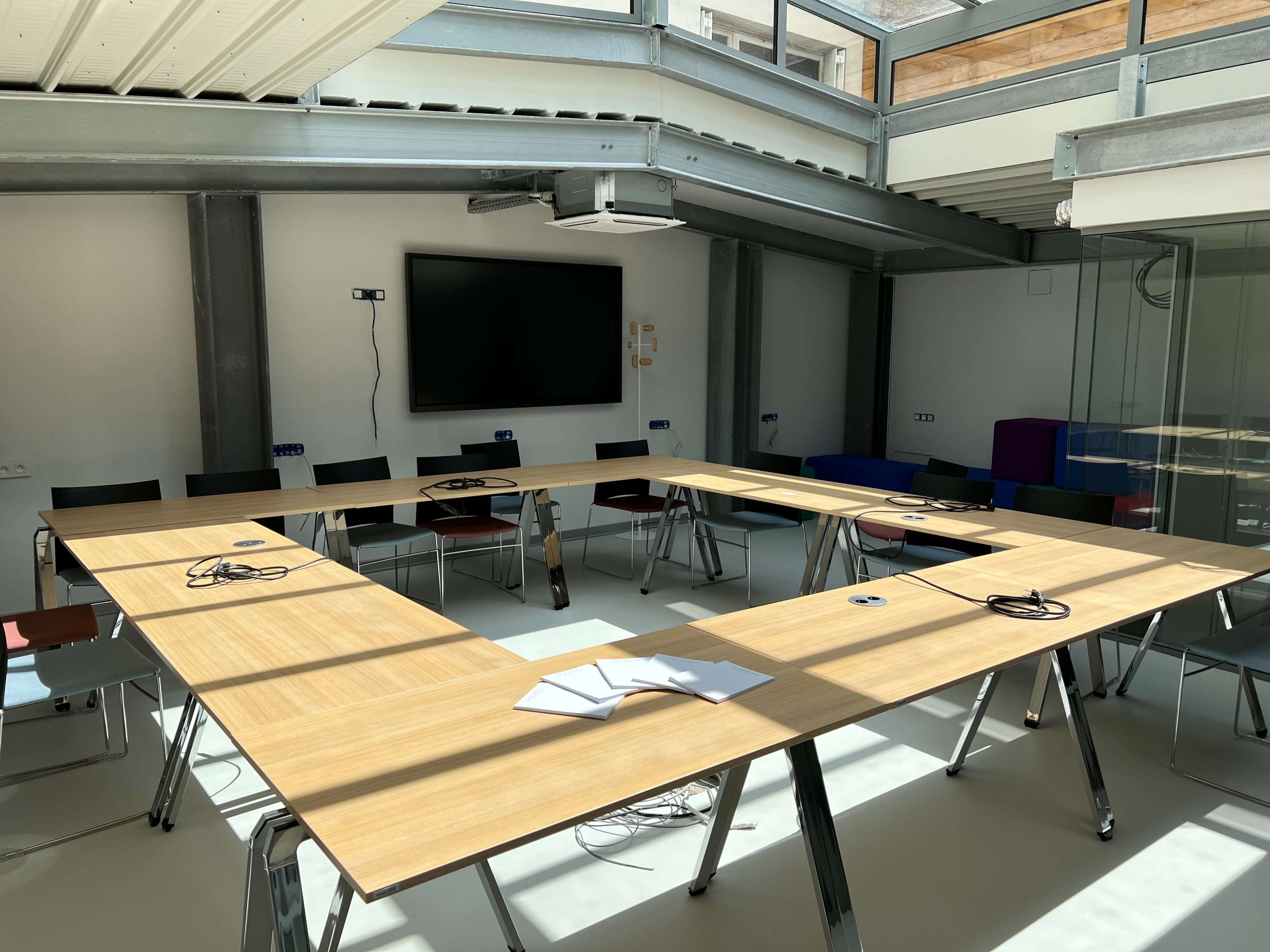 A large conference room features a rectangular table arranged in a U-shape, with chairs and a wall-mounted television.