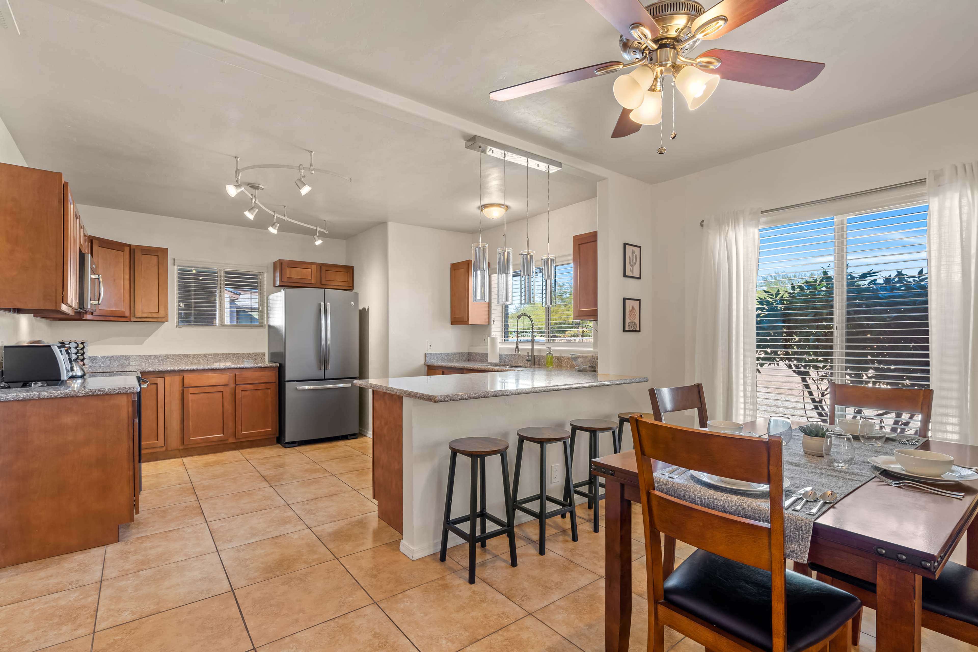 A modern kitchen with wooden cabinets, stainless steel appliances, a central island with bar stools, and a dining table set for a meal.
