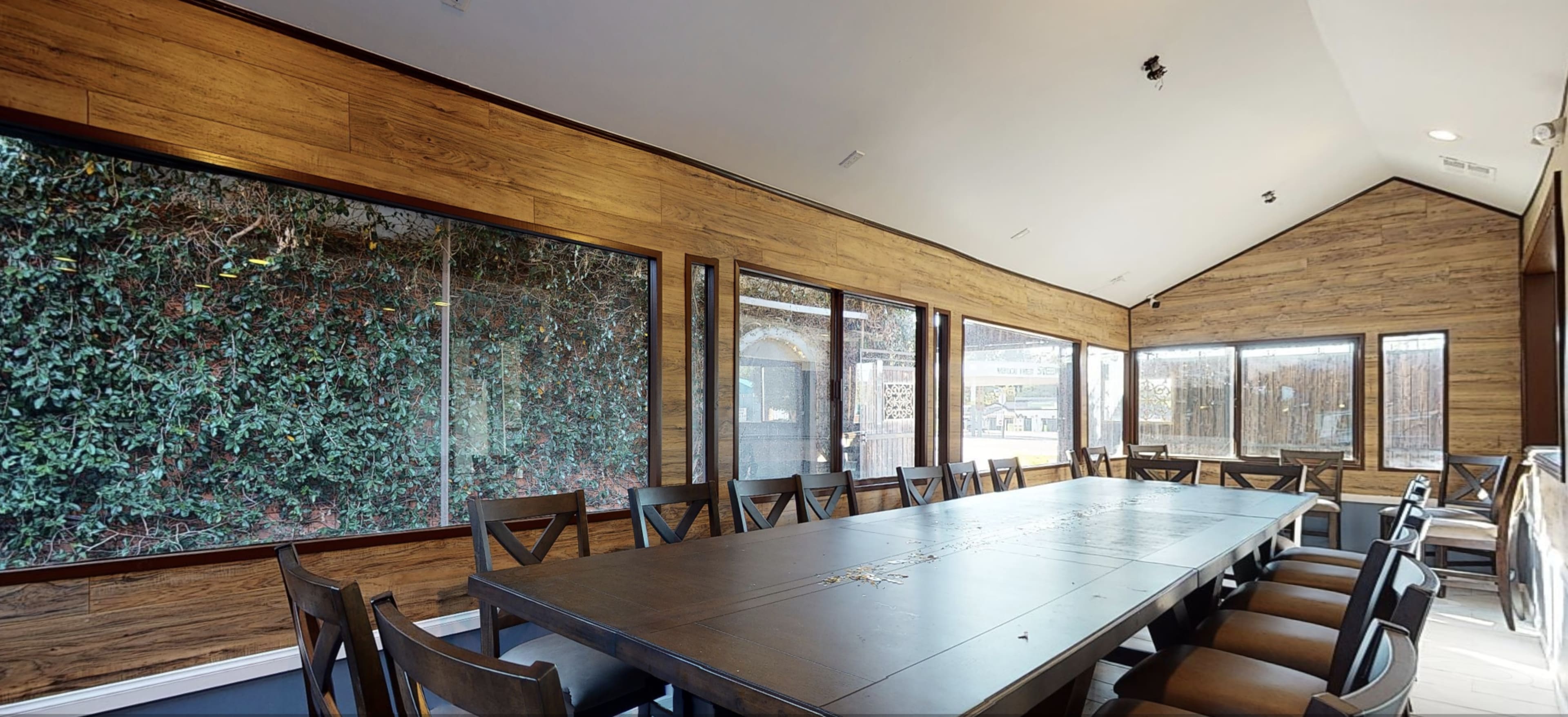 A spacious meeting room features a long table surrounded by chairs, with large windows overlooking a wall of greenery.