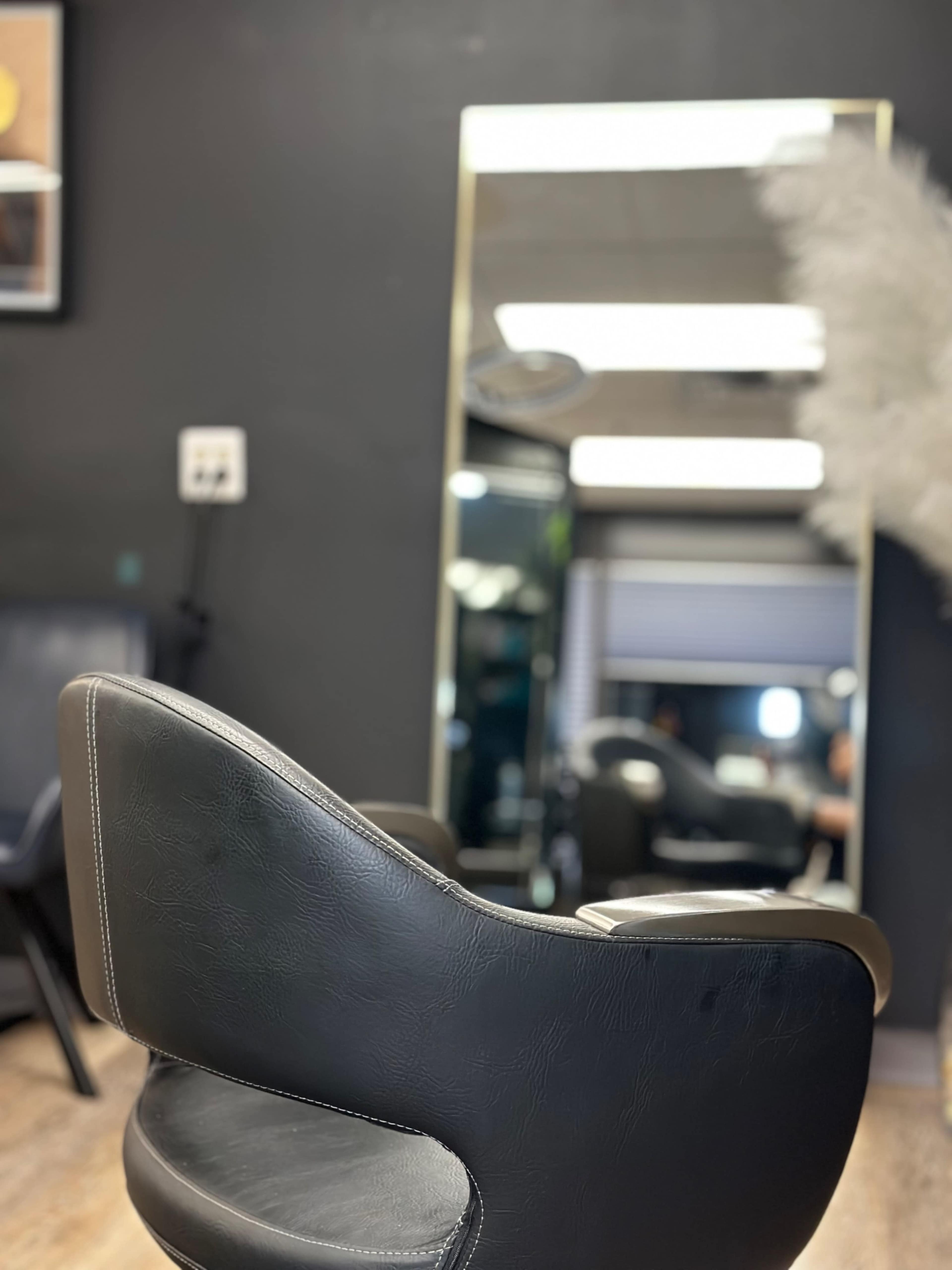 A black salon chair is positioned in front of a large mirror in a dimly lit hair salon.
