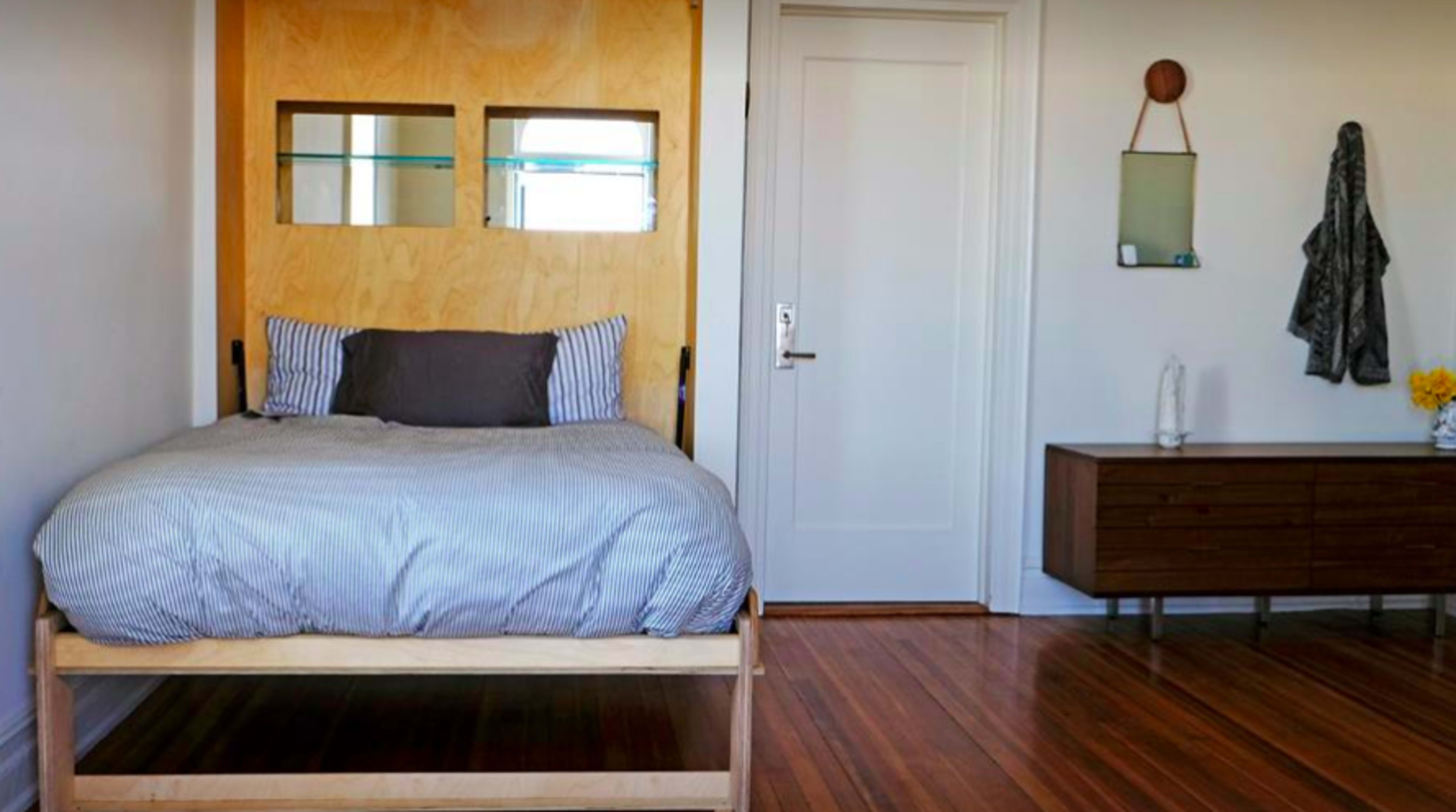 The image shows a bedroom with a wooden bed frame, a dresser, and a mirror mounted on the wall.