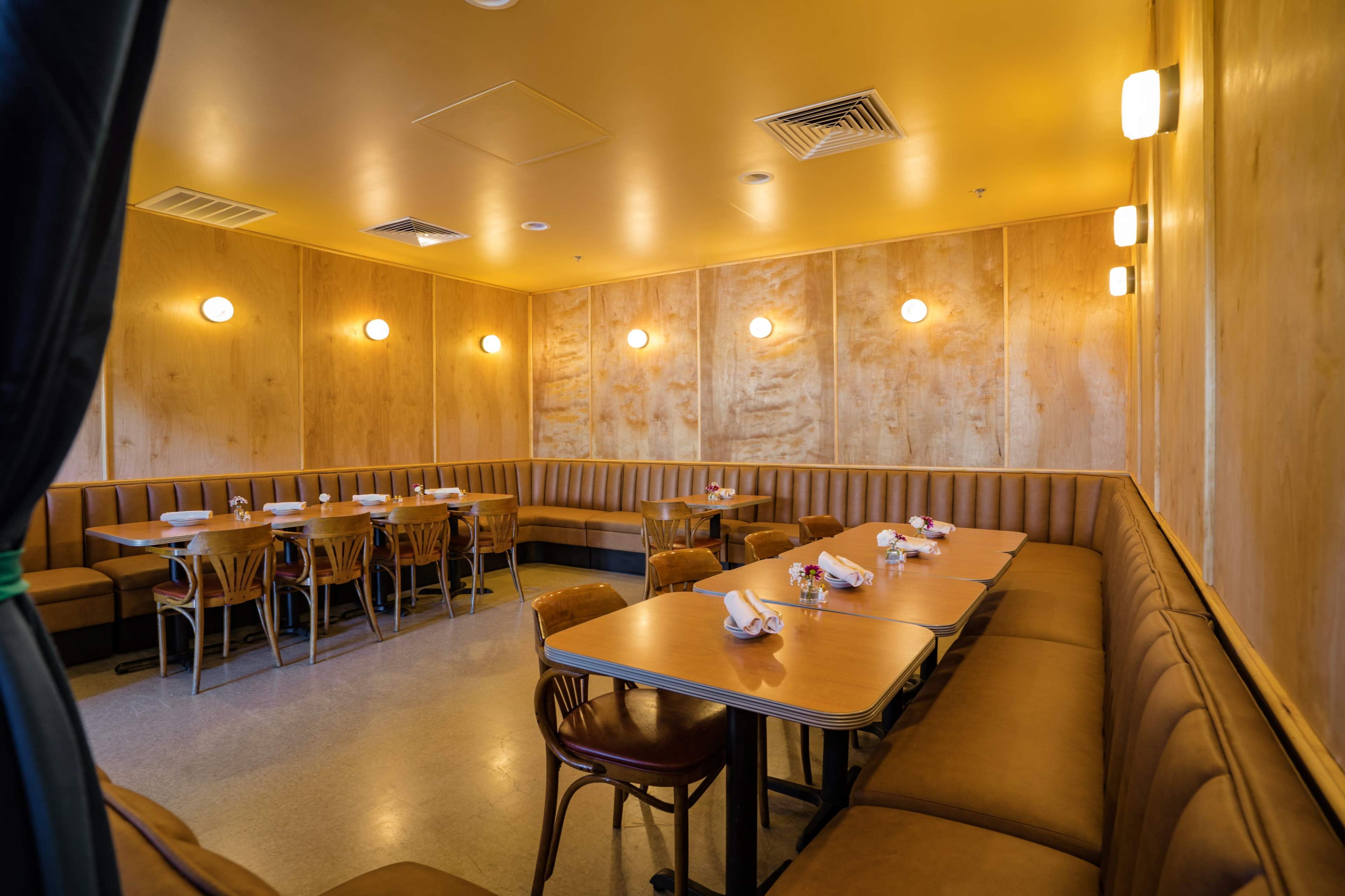 The image shows a modern restaurant interior with wooden paneling, neatly set tables, and cozy booth seating arranged against the walls.