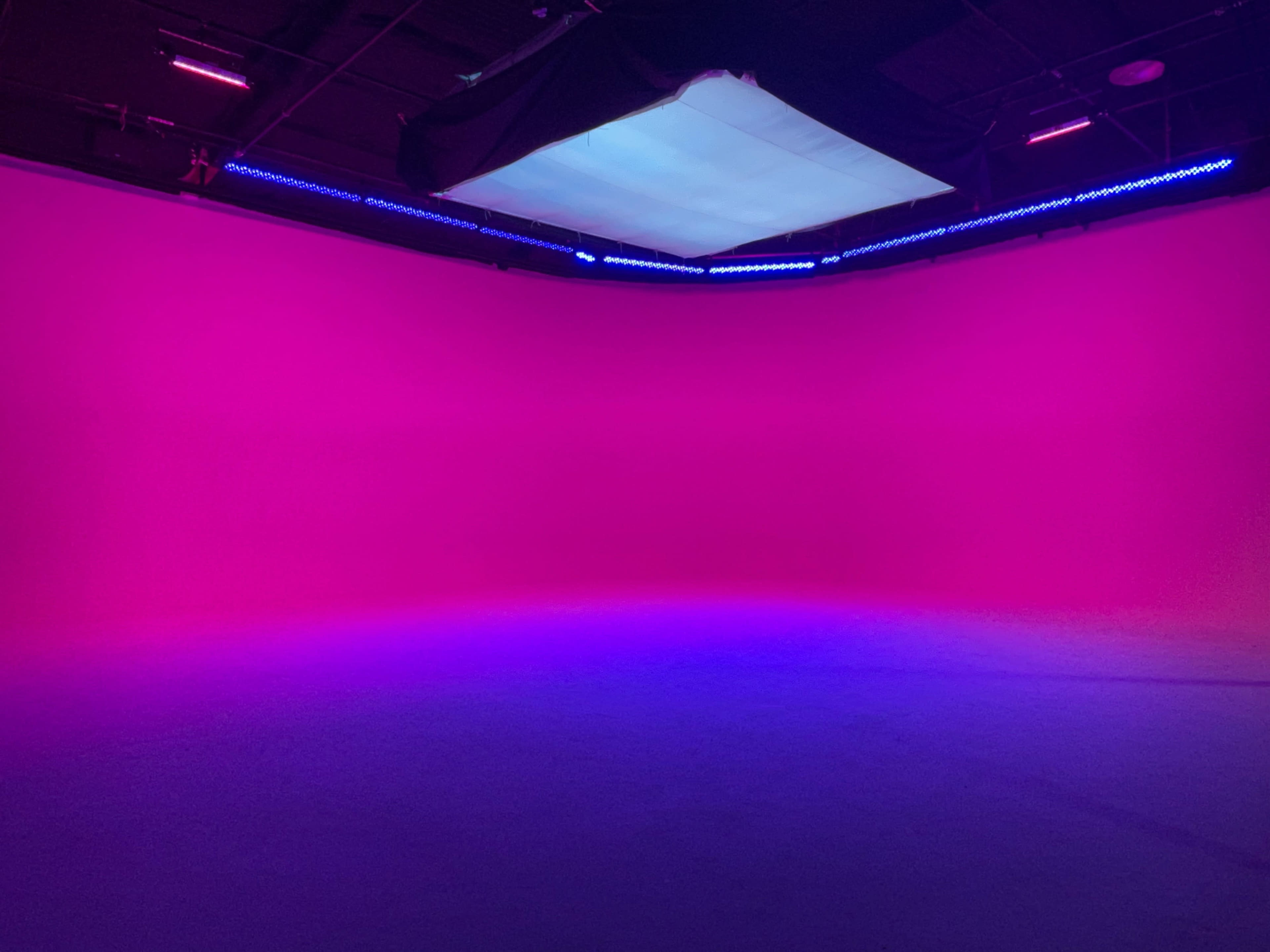 A studio space with a seamless pink backdrop illuminated by blue and purple lighting.