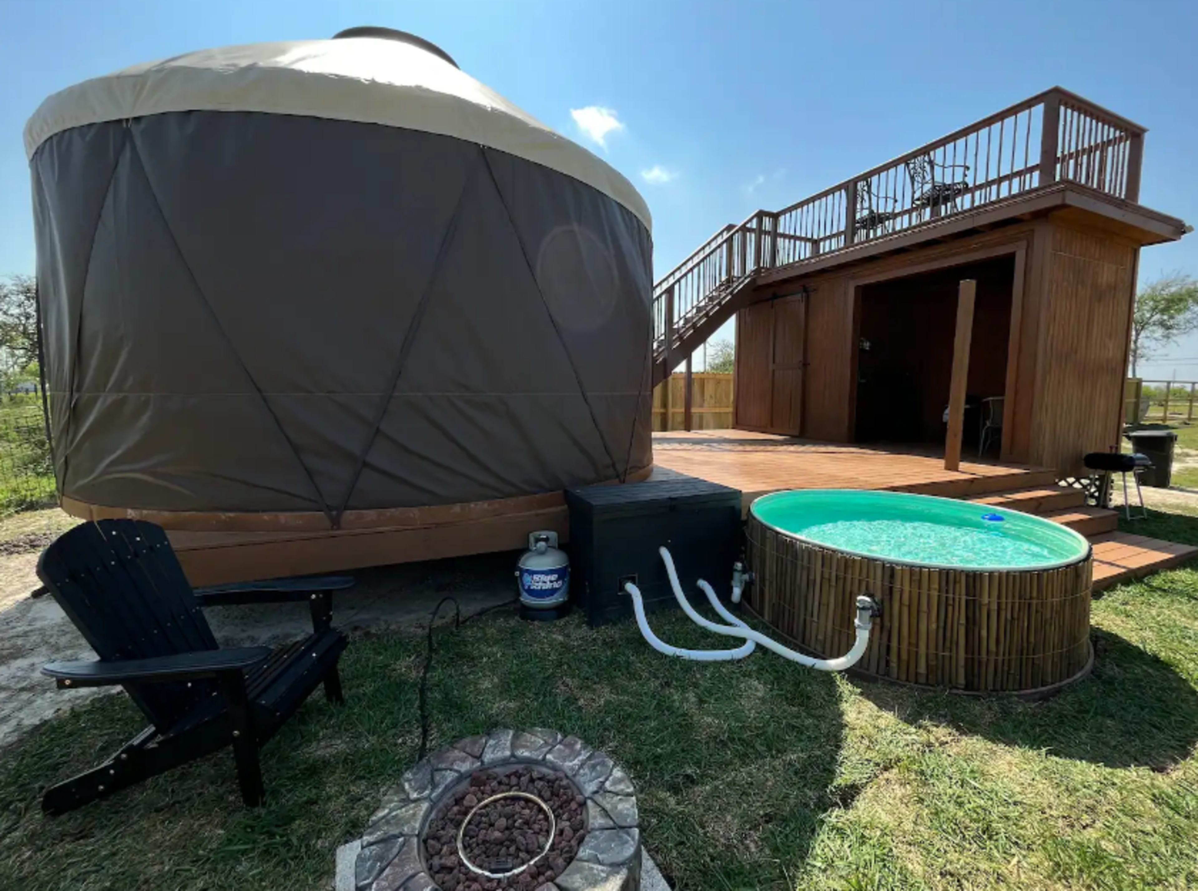 A yurt with a deck and a small above-ground hot tub next to it, set in a grassy outdoor area.