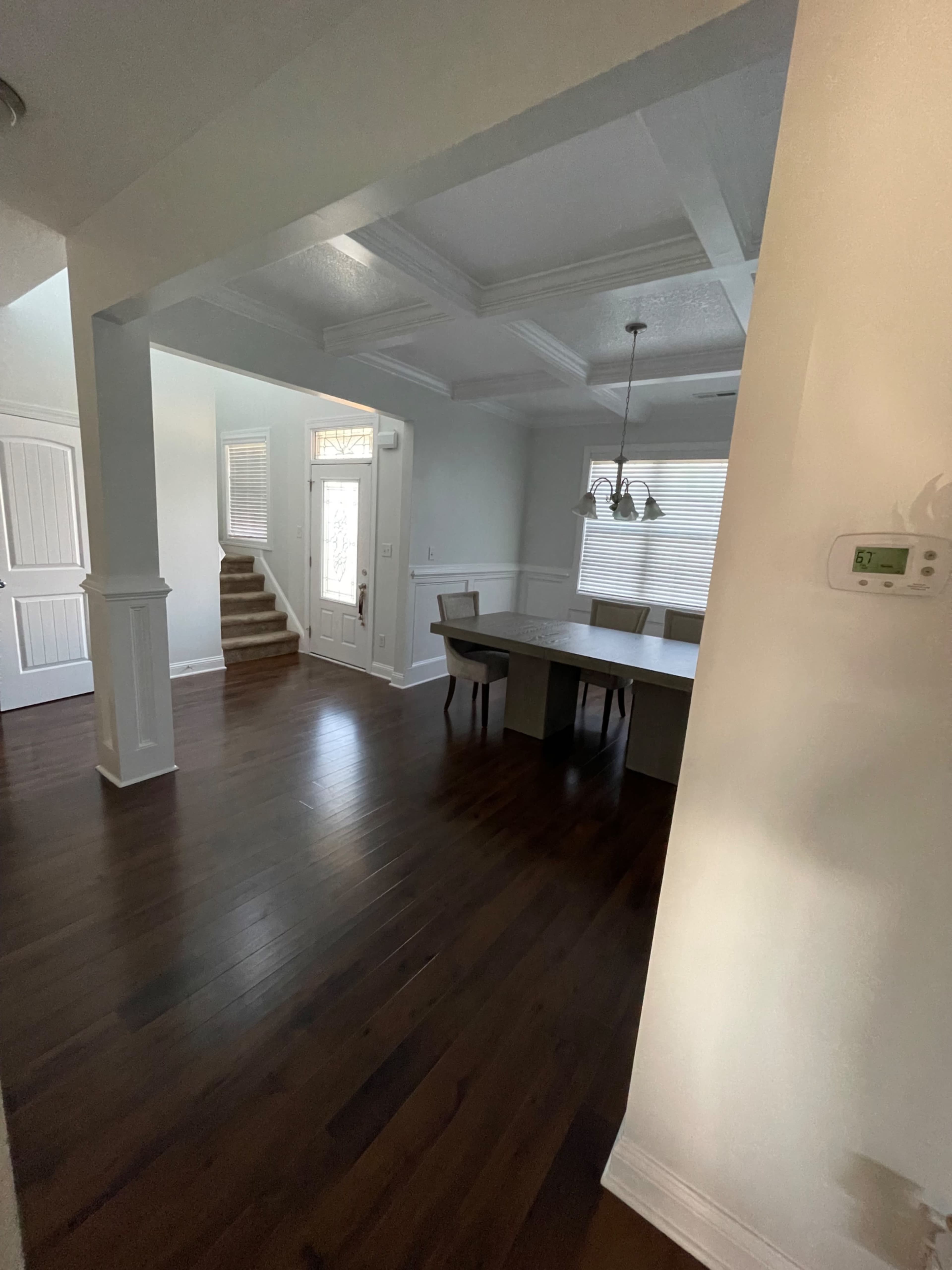A spacious dining area with a long table and chairs, connected to a staircase and a front door, all featuring wooden flooring.