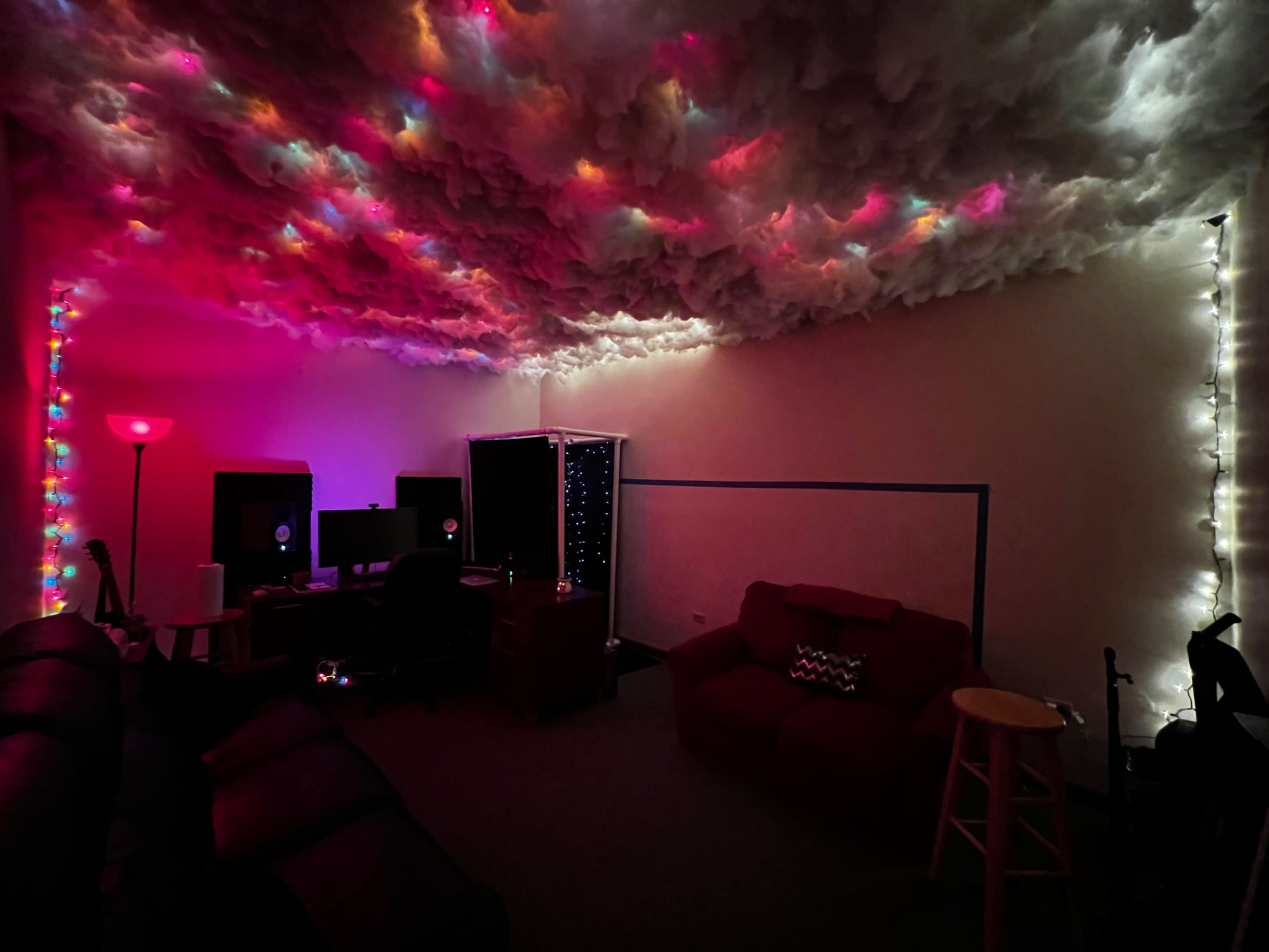 The room features a ceiling designed to resemble clouds, illuminated by colorful lights, with two computers on desks and various seating areas.