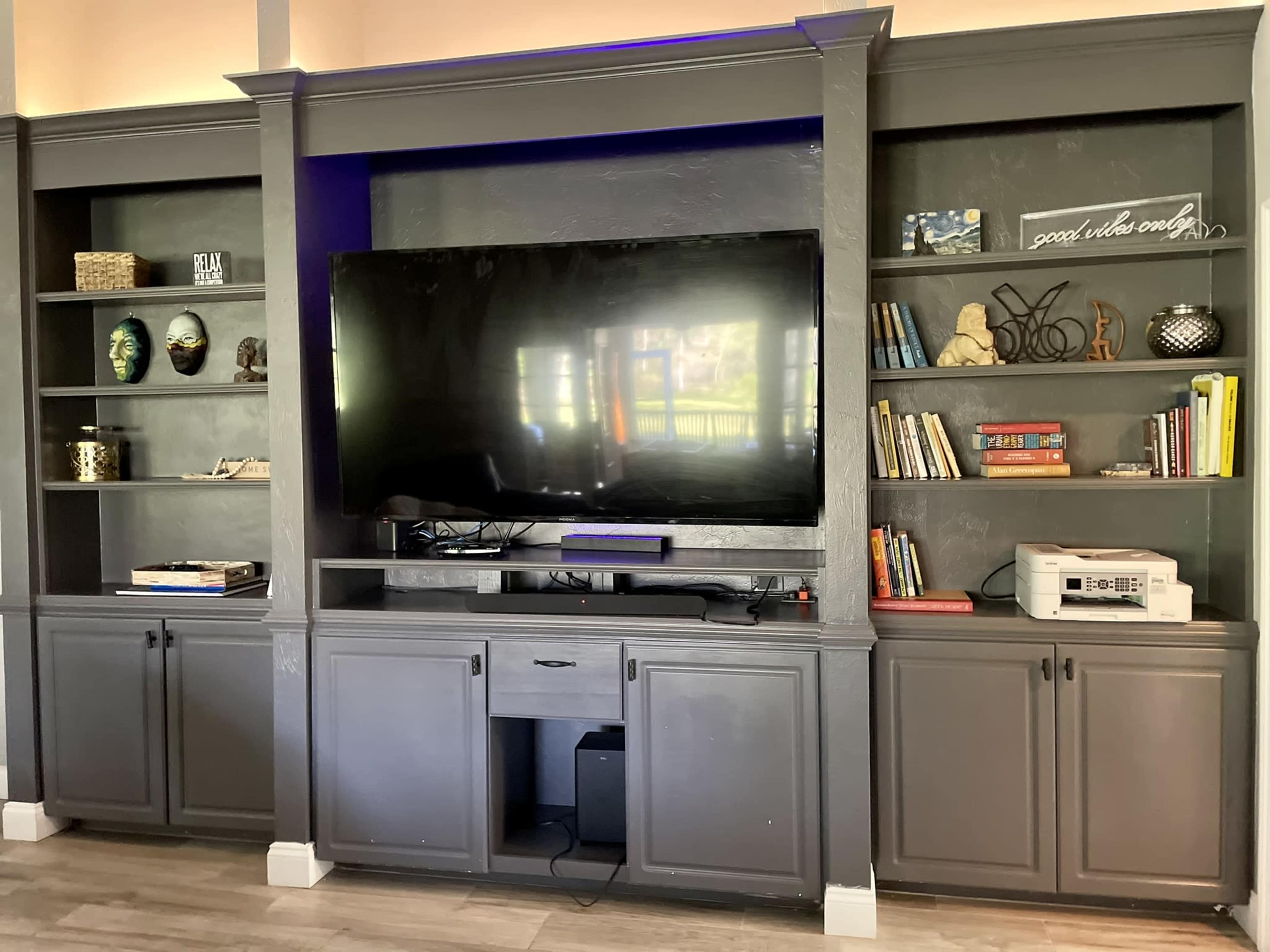 A living room wall unit featuring a large television, shelves with decorative items and books, and a cabinet below for storage.