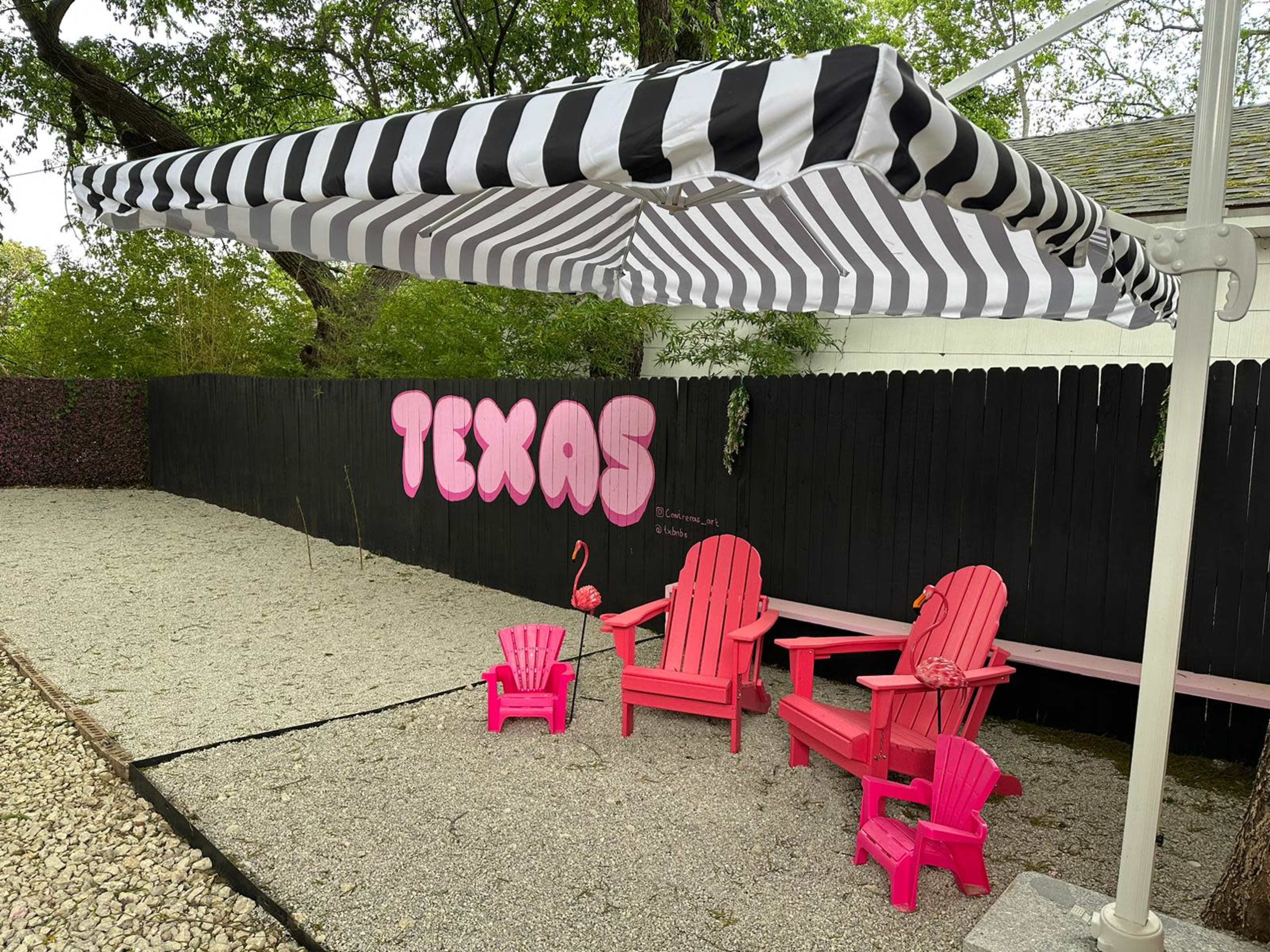 A shaded area features pink Adirondack chairs and a flamingo statue in front of a black fence with "TEXAS" painted on it.