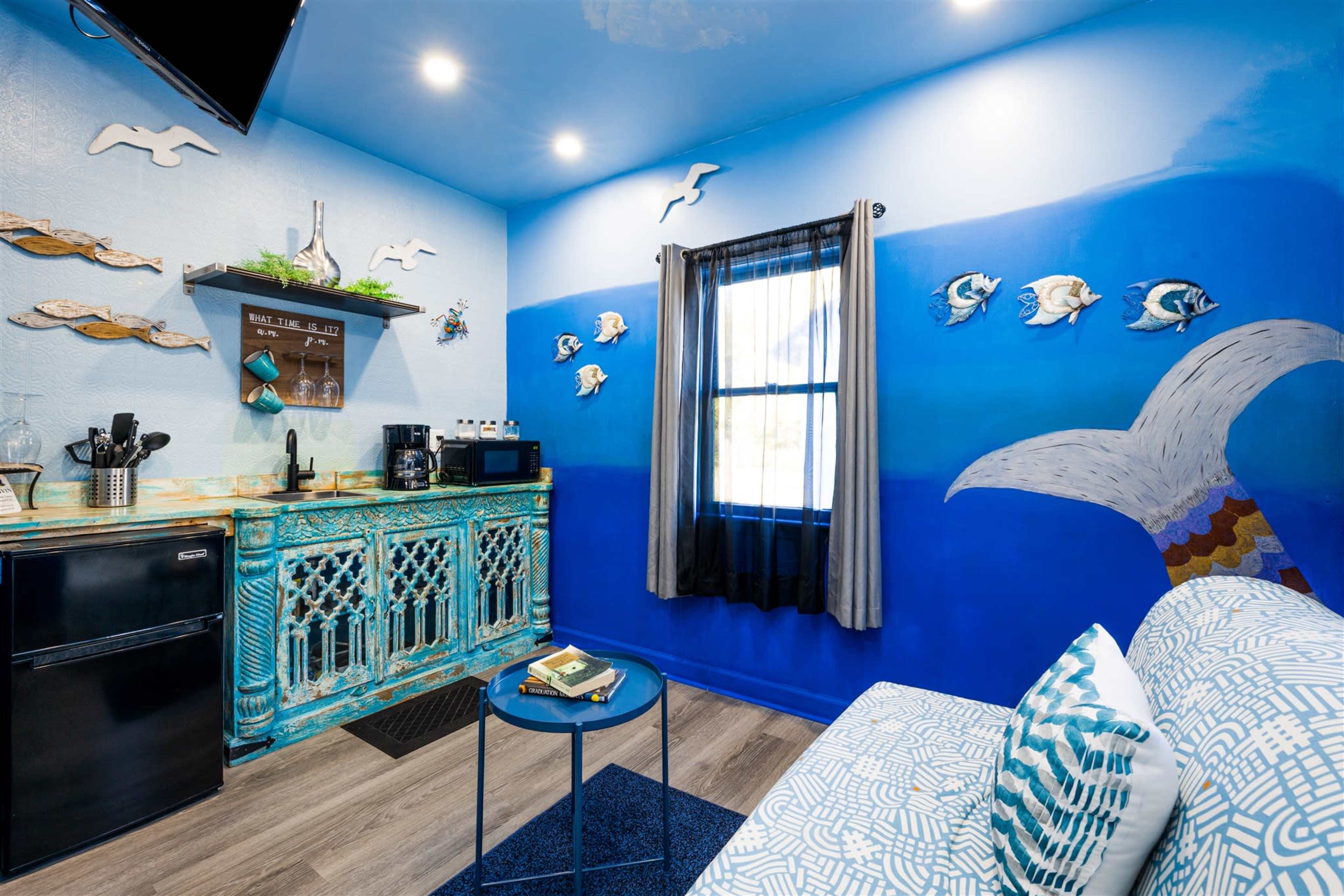 A small room with blue walls, a kitchenette featuring a turquoise cabinet, and decorative fish on the walls.