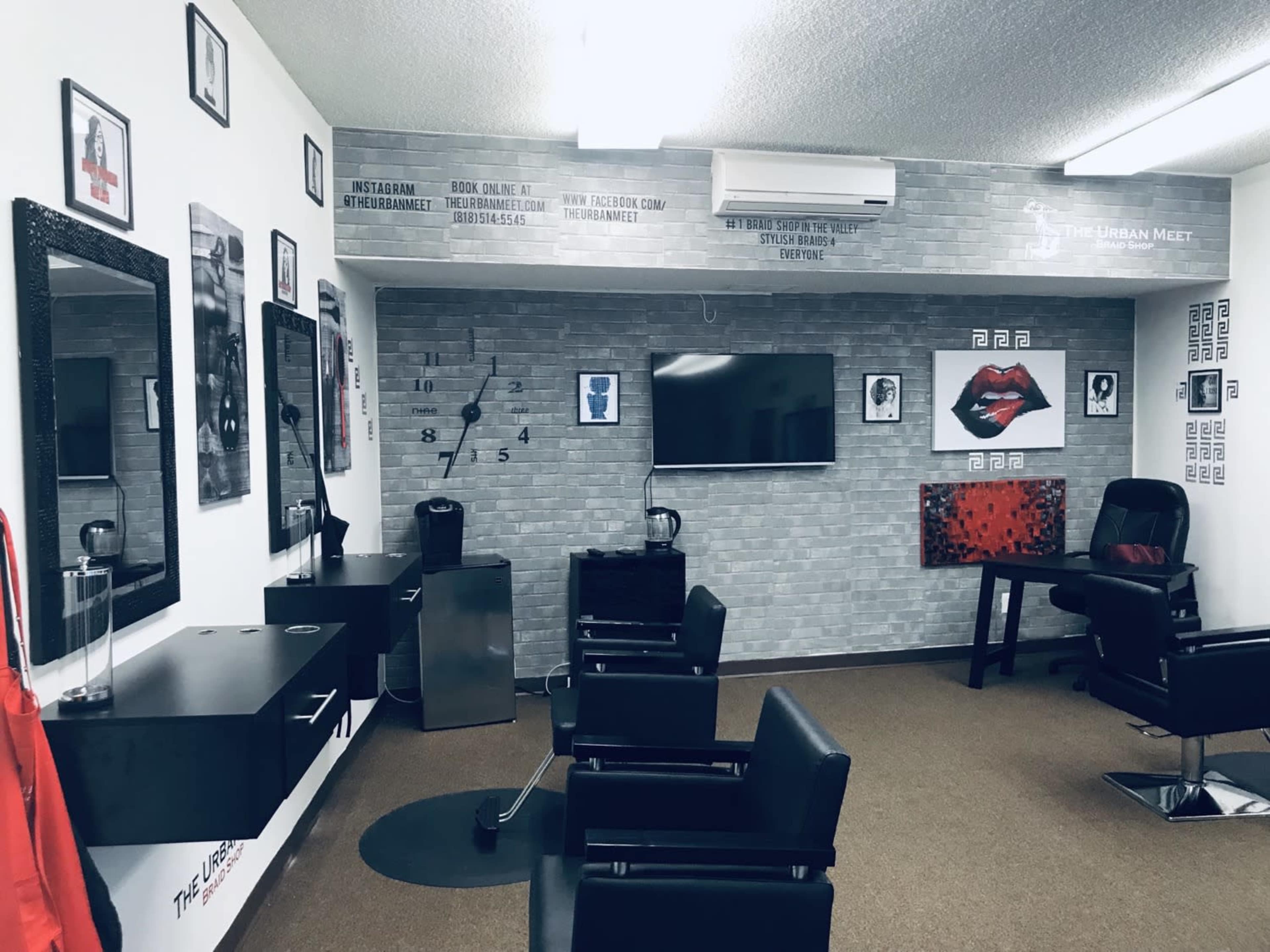 A modern salon interior featuring black styling chairs, large mirrors, a television, and various wall decorations.