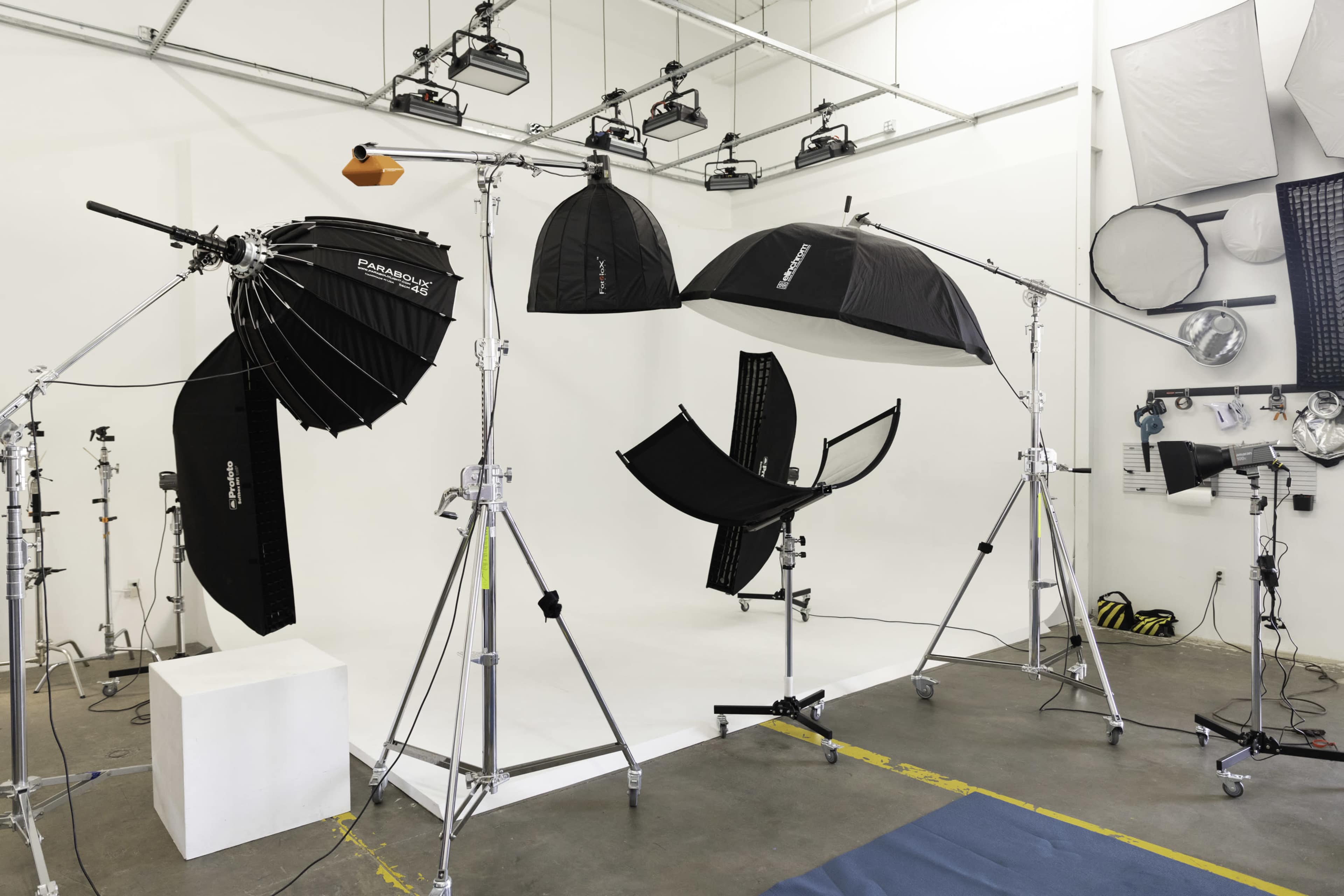 A photography studio setup with various lighting equipment, including softboxes and umbrellas, arranged around a white backdrop.