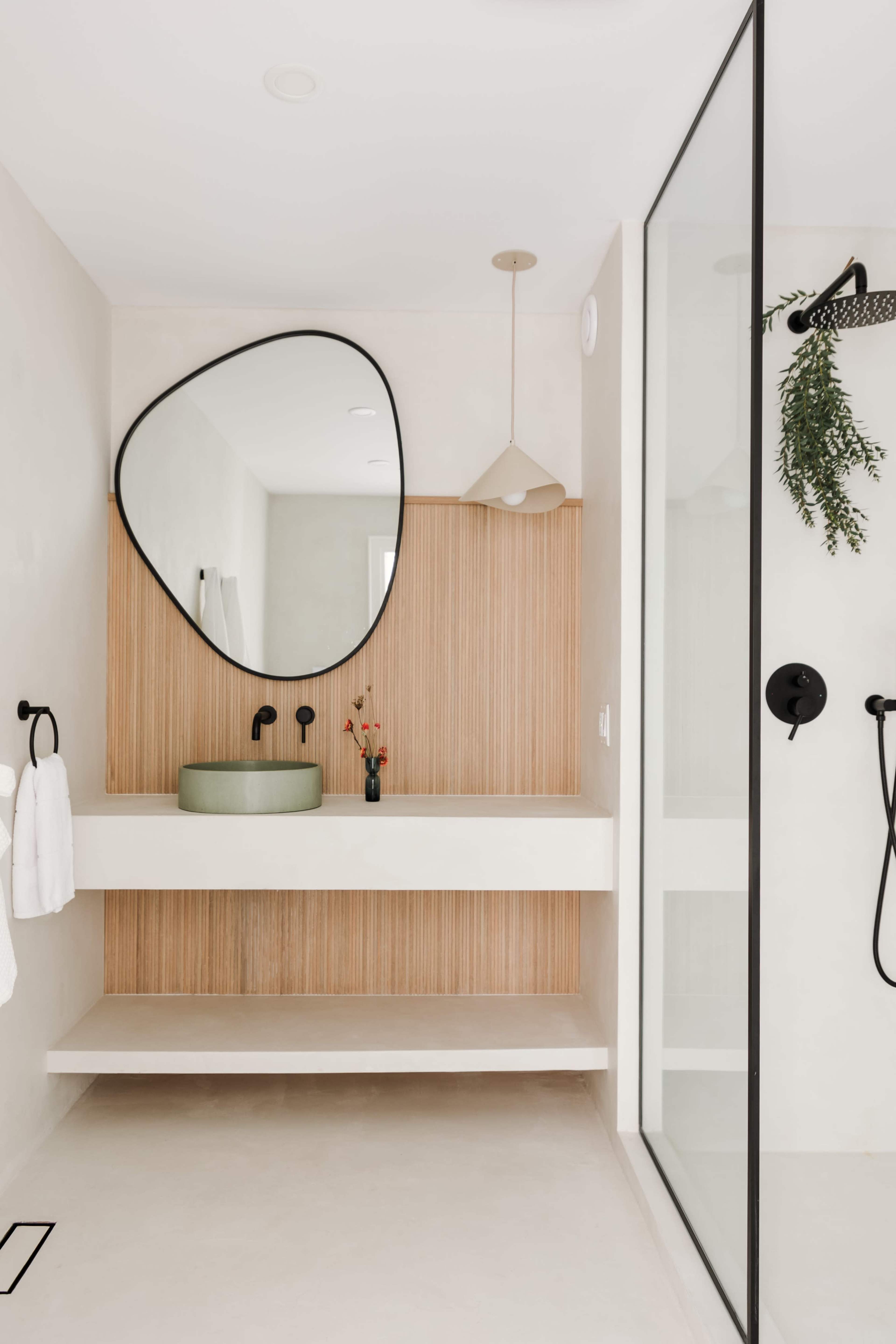 A modern bathroom featuring a green basin on a floating countertop, a large mirror, and a glass shower enclosure.
