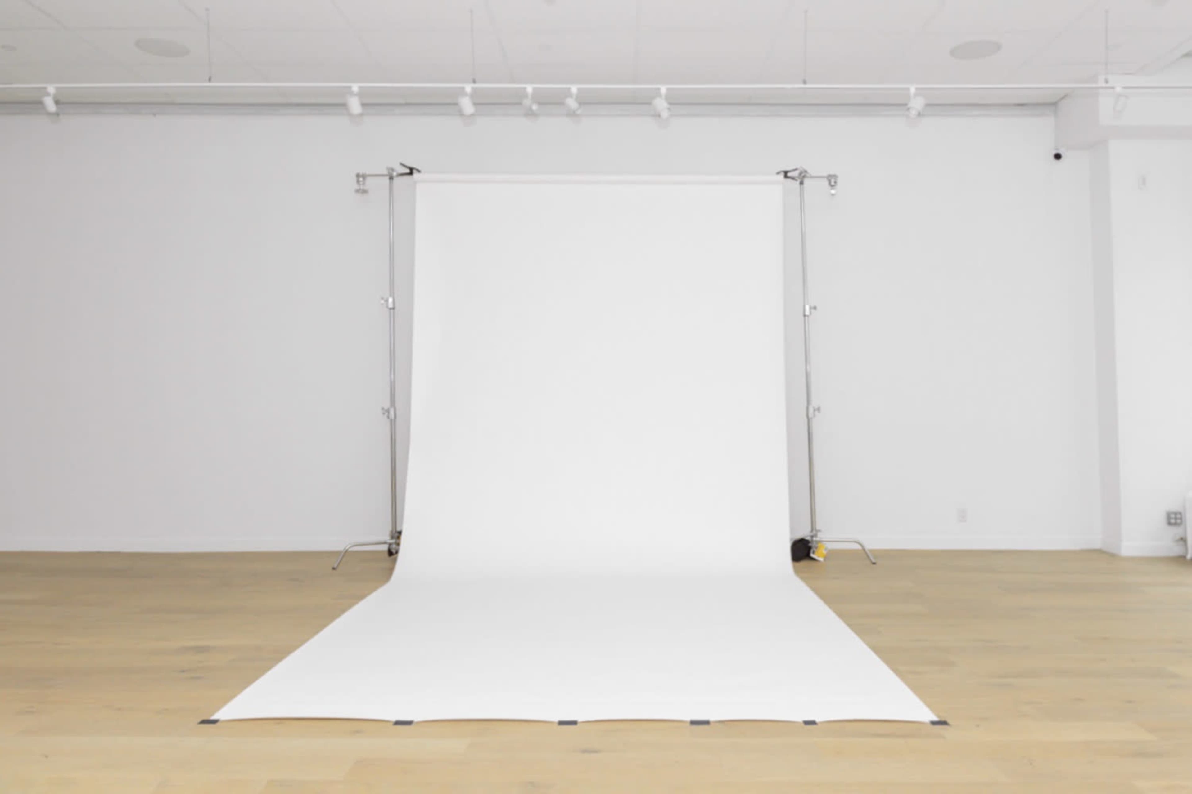 The image shows a spacious, well-lit studio featuring a white backdrop mounted on a frame with a smooth floor.