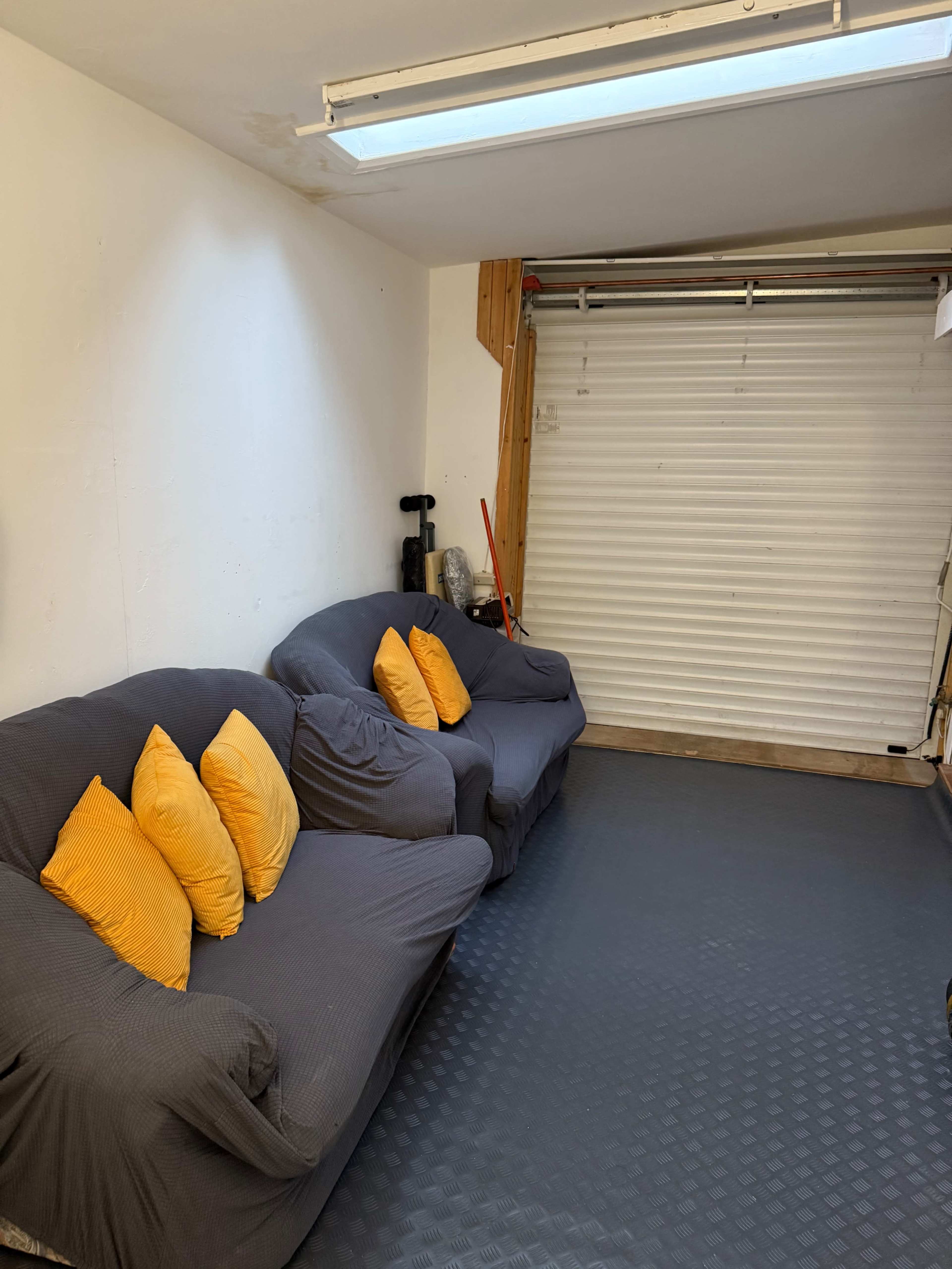 The image shows a garage or storage space with two gray sofas adorned with orange cushions, and a white roll-up door in the background.
