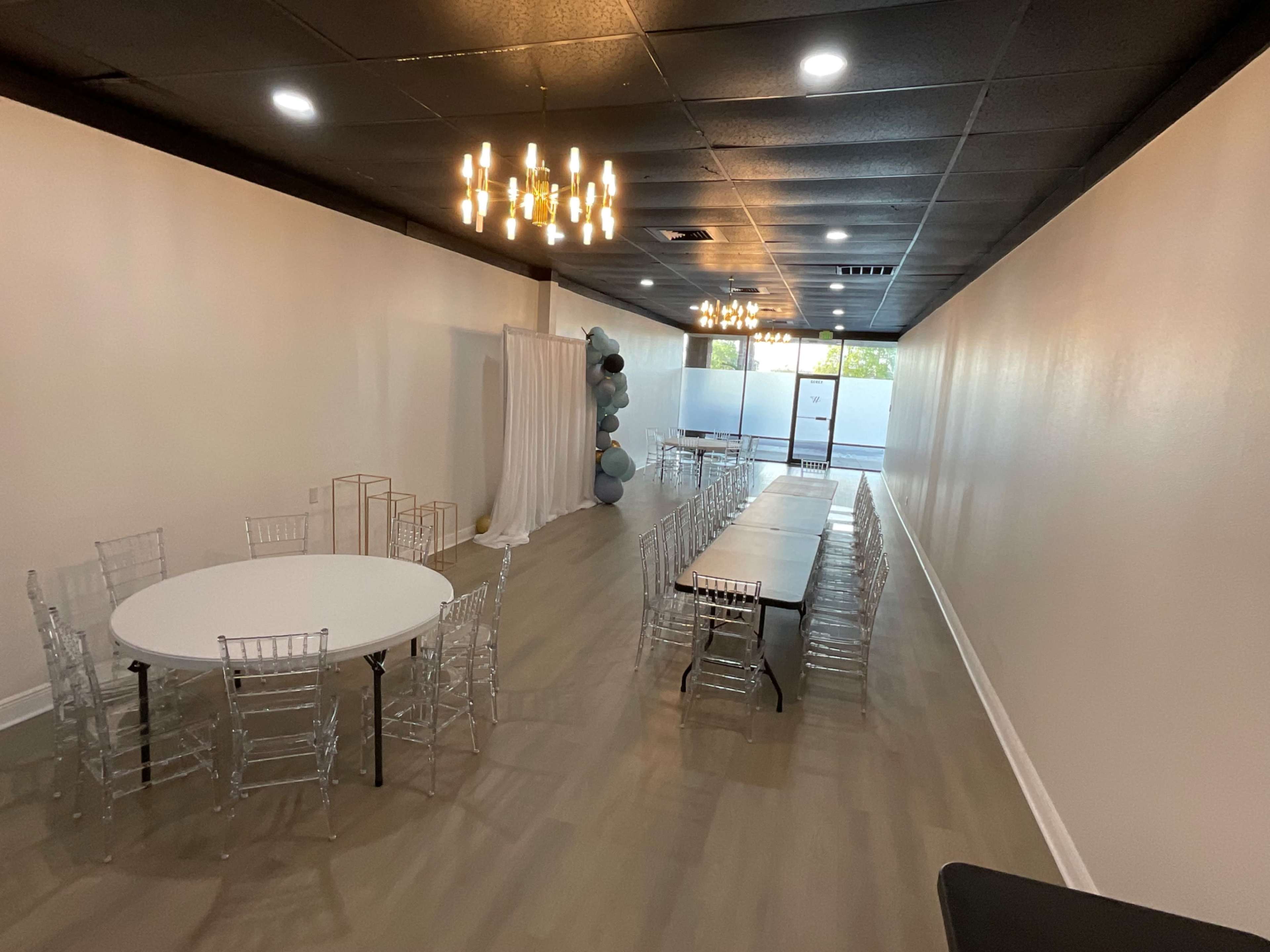 A spacious event room with a round table and a long rectangular table set up, along with decorative elements and another area for a backdrop.
