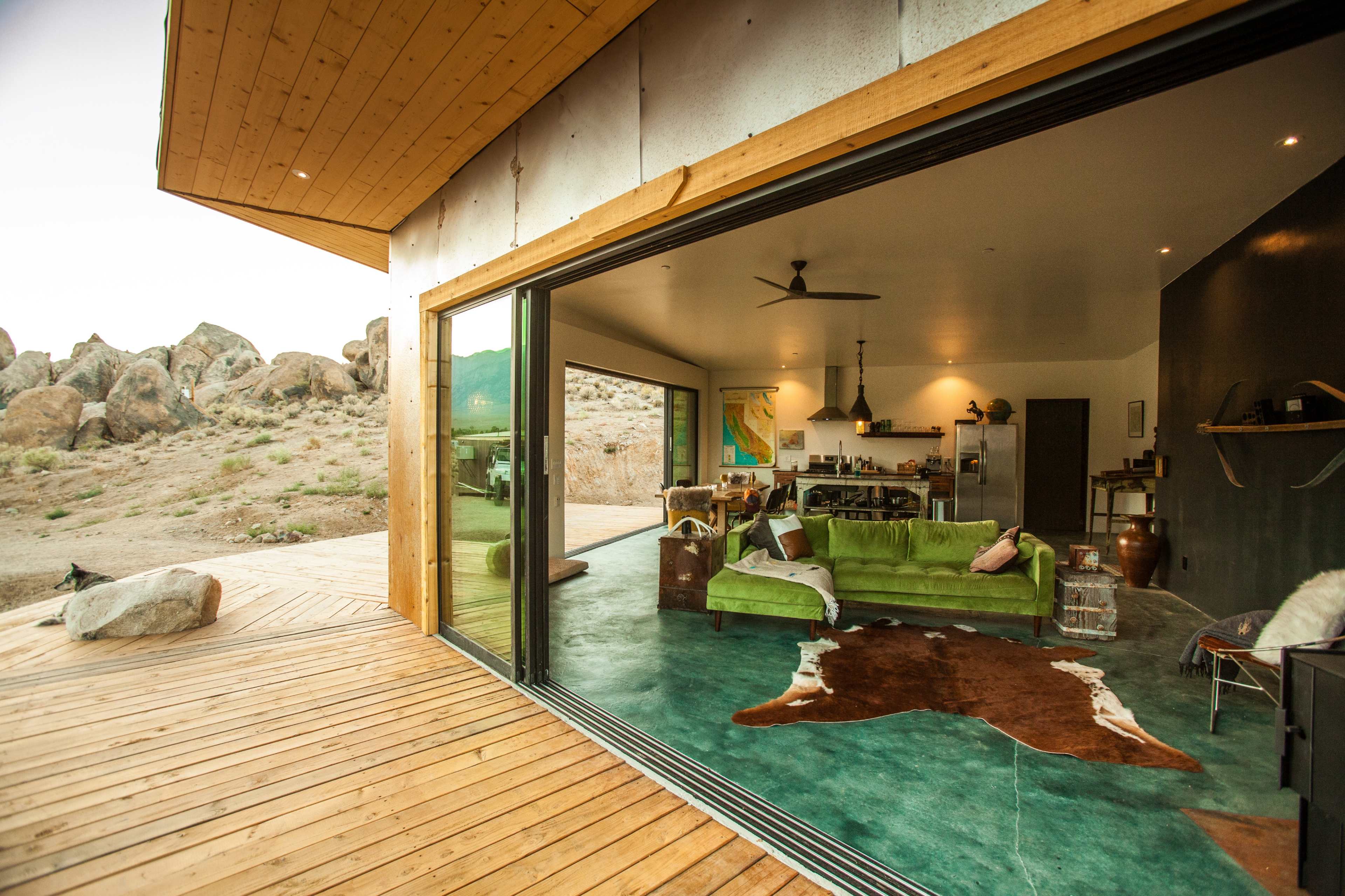 A modern living space with a green sofa, large glass doors, and a view of rocky terrain outside.