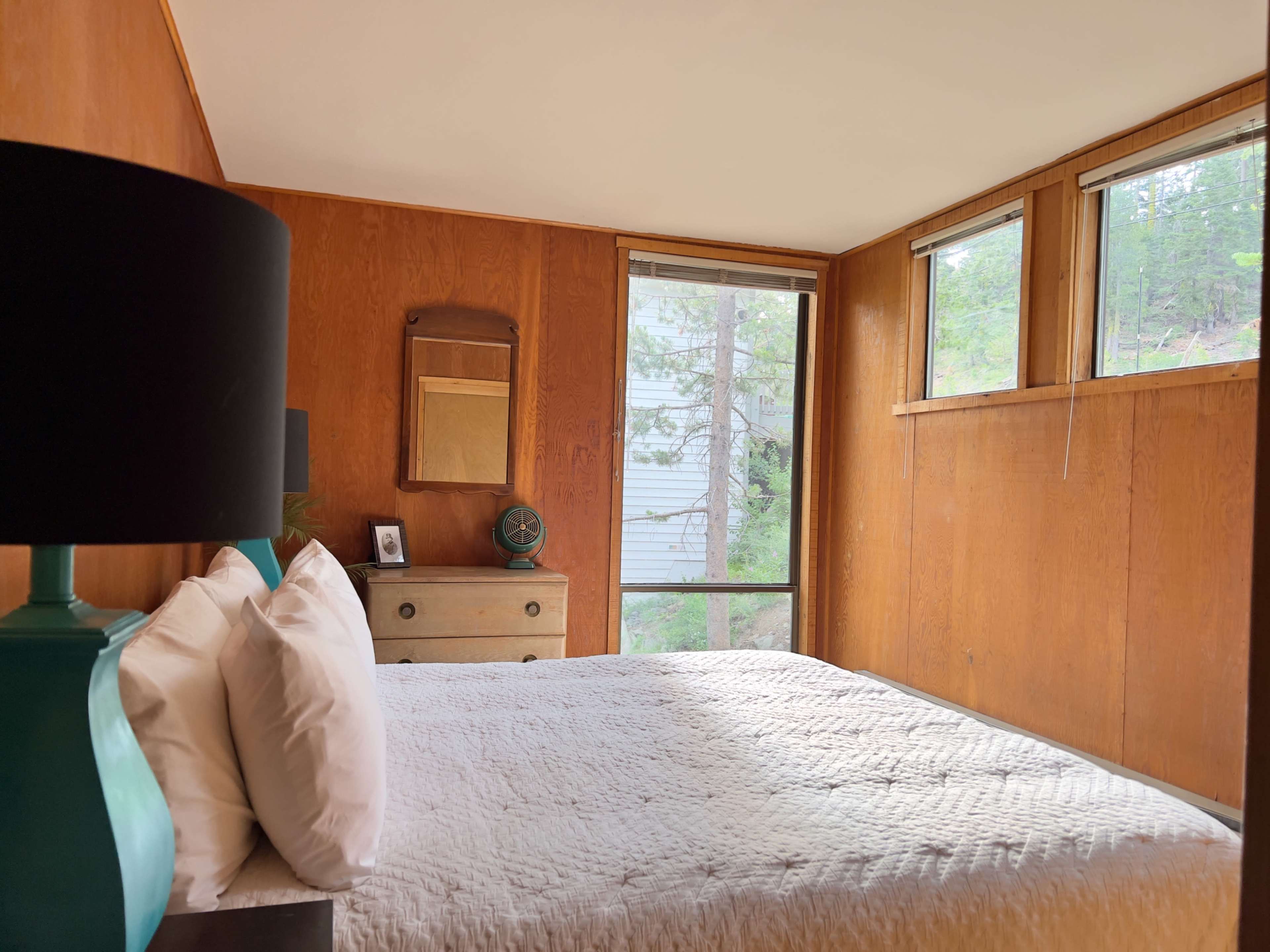 A bedroom with a bed, a dresser, and large windows allowing natural light to enter.