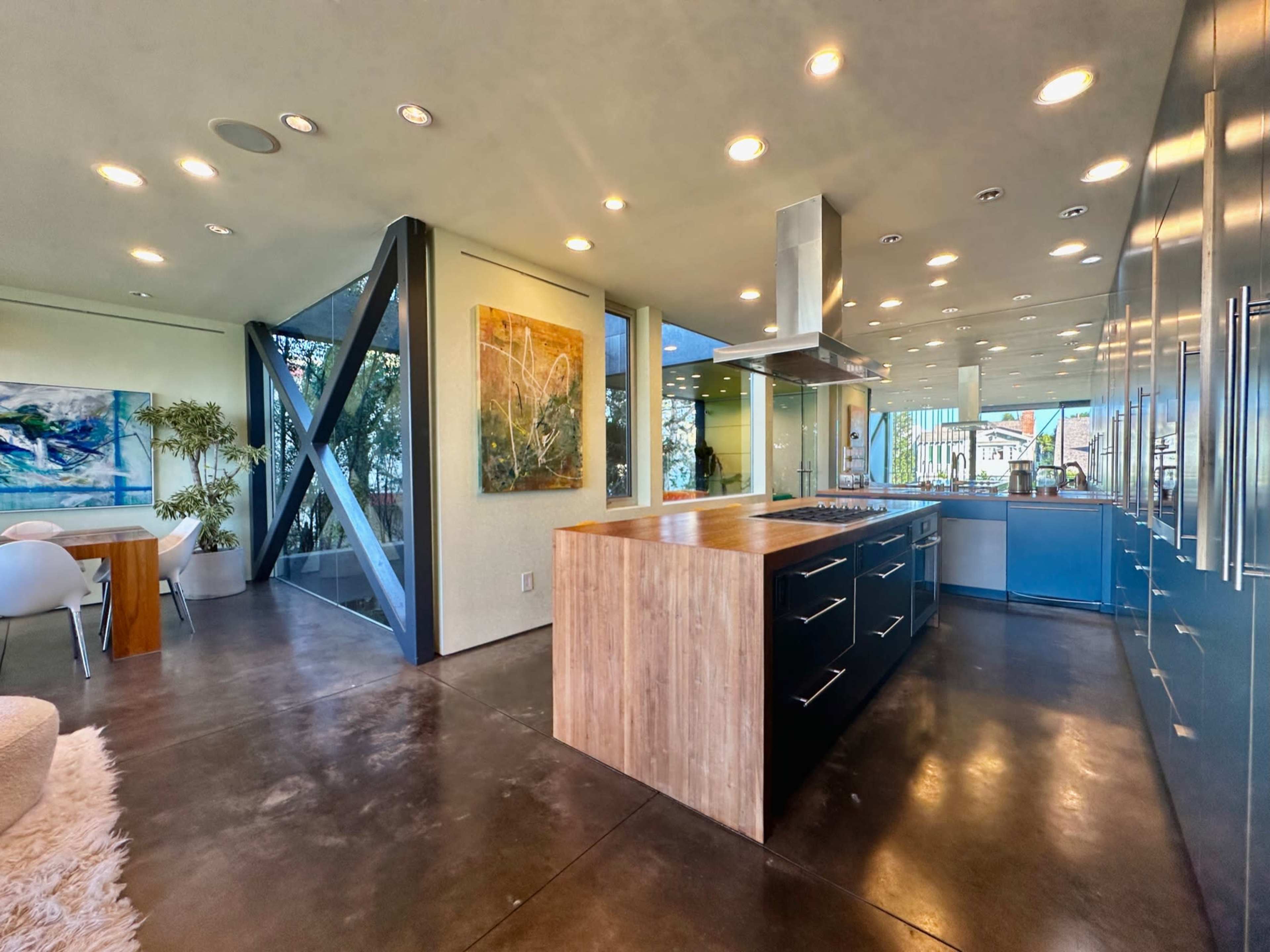 A modern kitchen features an island with a wooden countertop, sleek cabinetry, and large windows offering views of the outdoors.