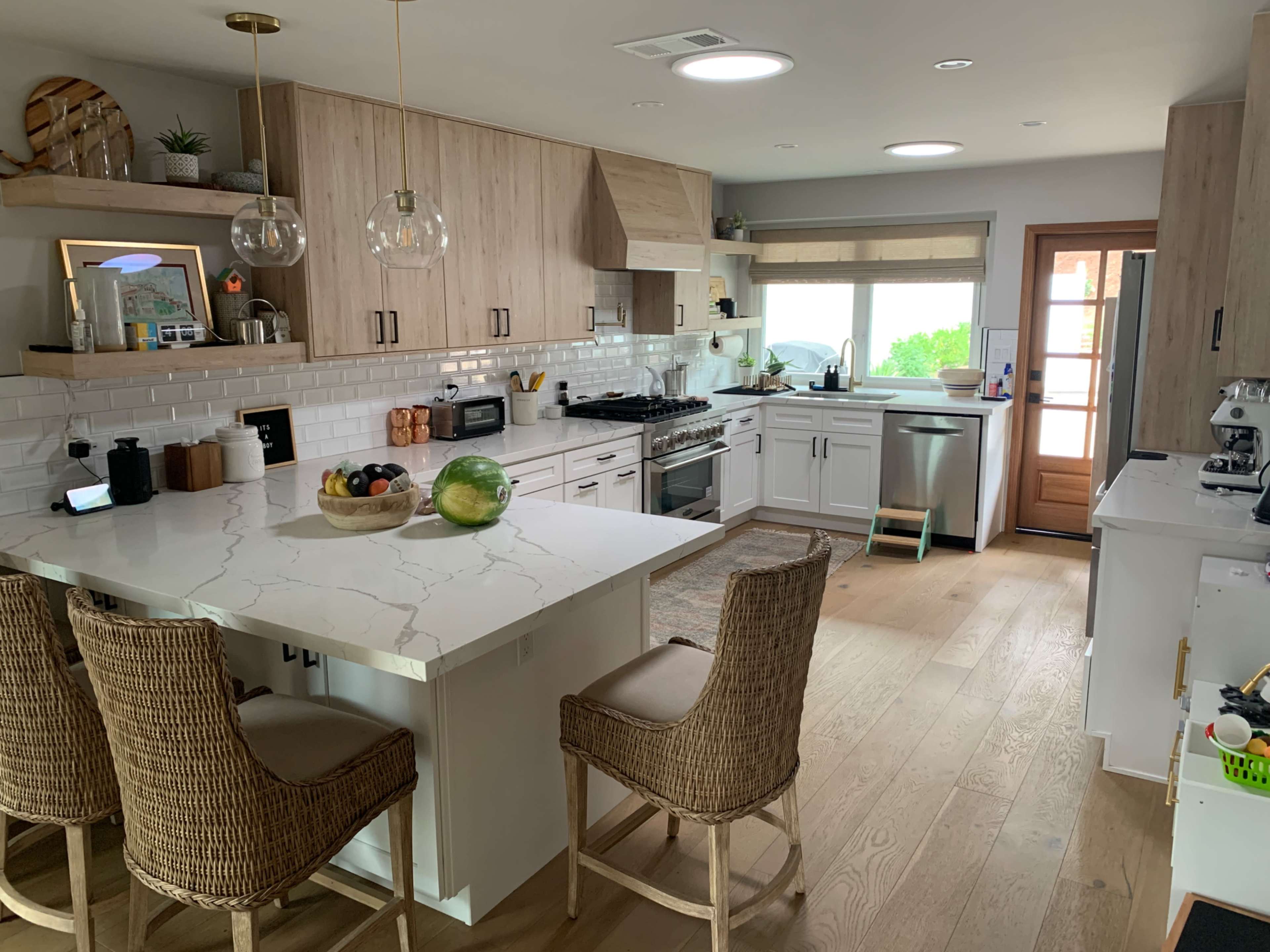 A modern kitchen features white cabinetry, a marble countertop island with bar stools, and large windows allowing natural light.