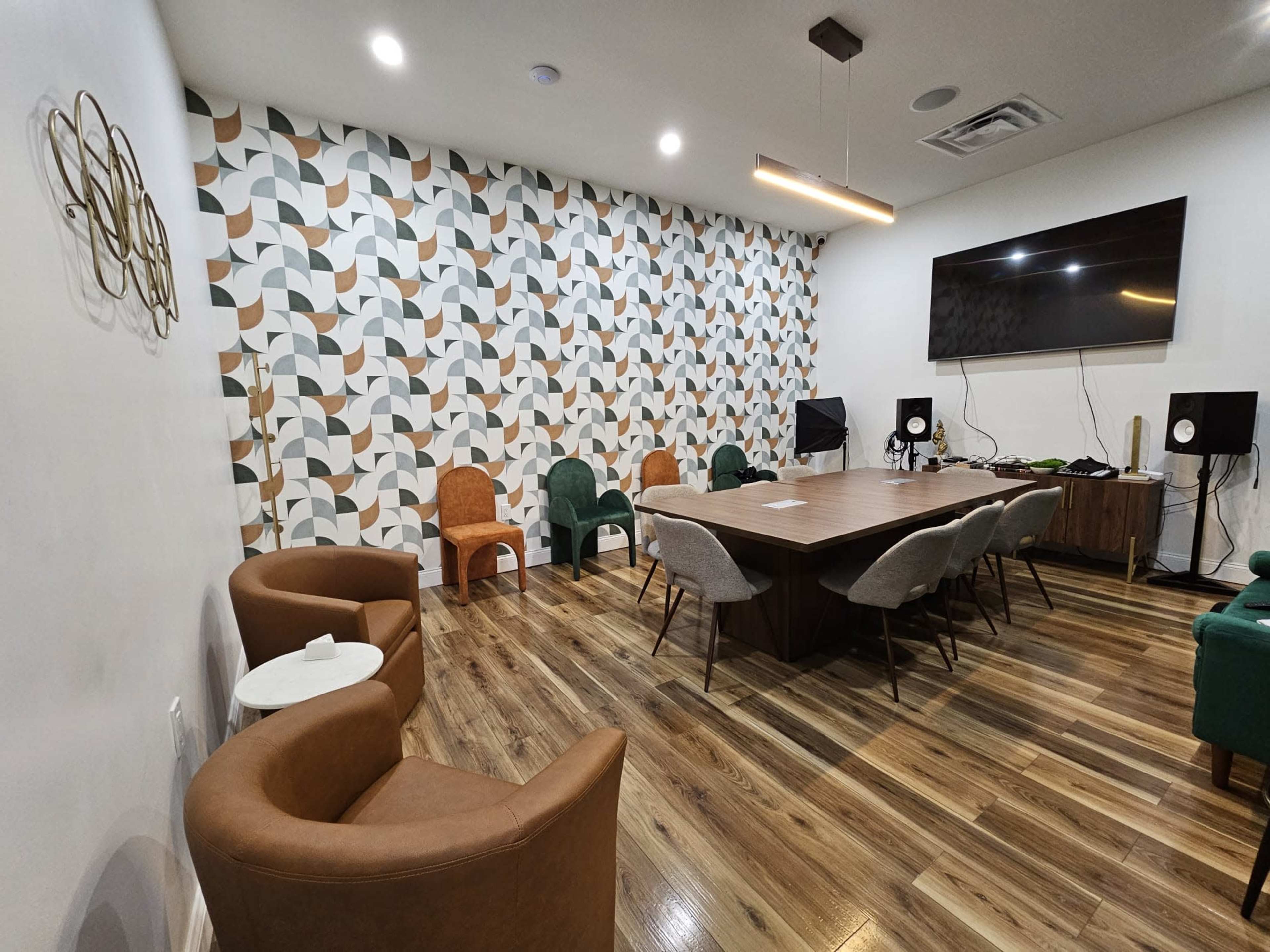 A meeting room with a large wooden table surrounded by various chairs, a television on the wall, and a geometric patterned wallpaper.