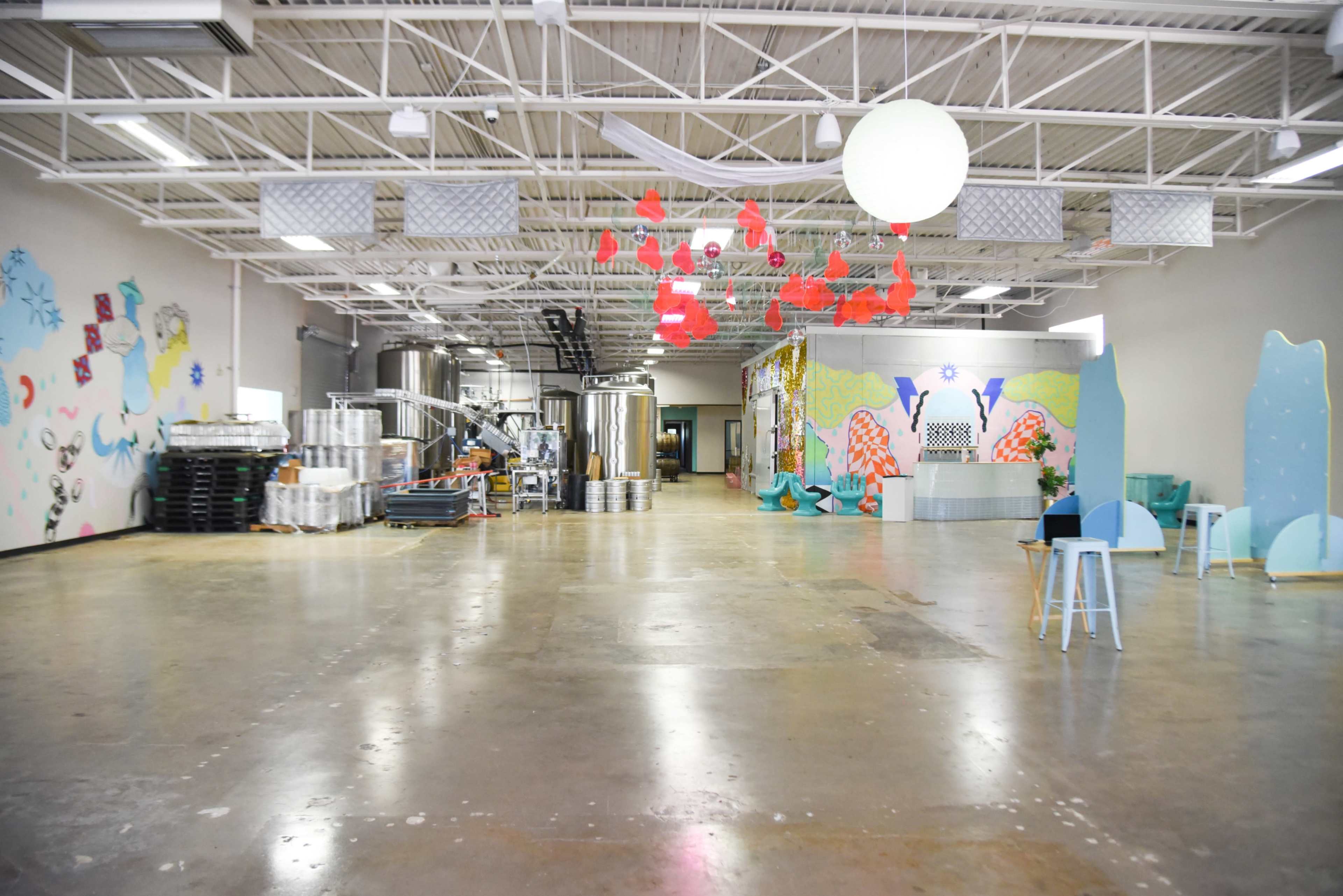 An empty, industrial-style space with large metal tanks on one side and vibrant wall art on the opposite wall.