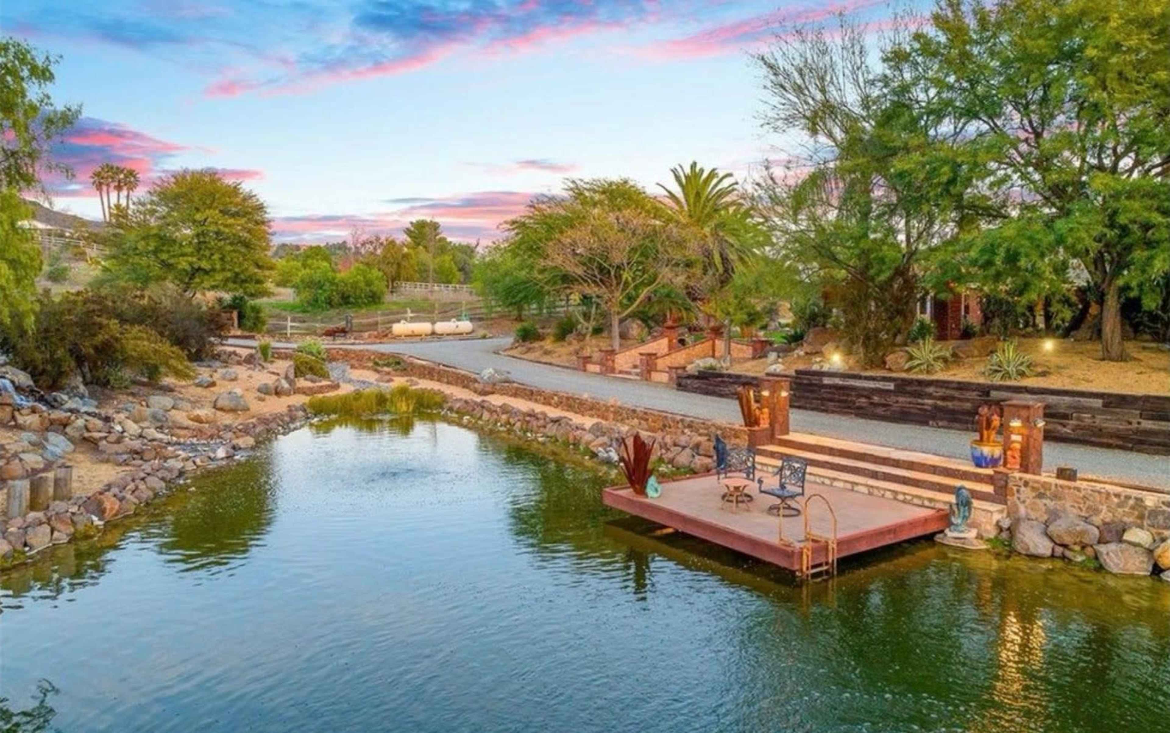 The image shows a tranquil pond surrounded by greenery and a wooden dock with seating.
