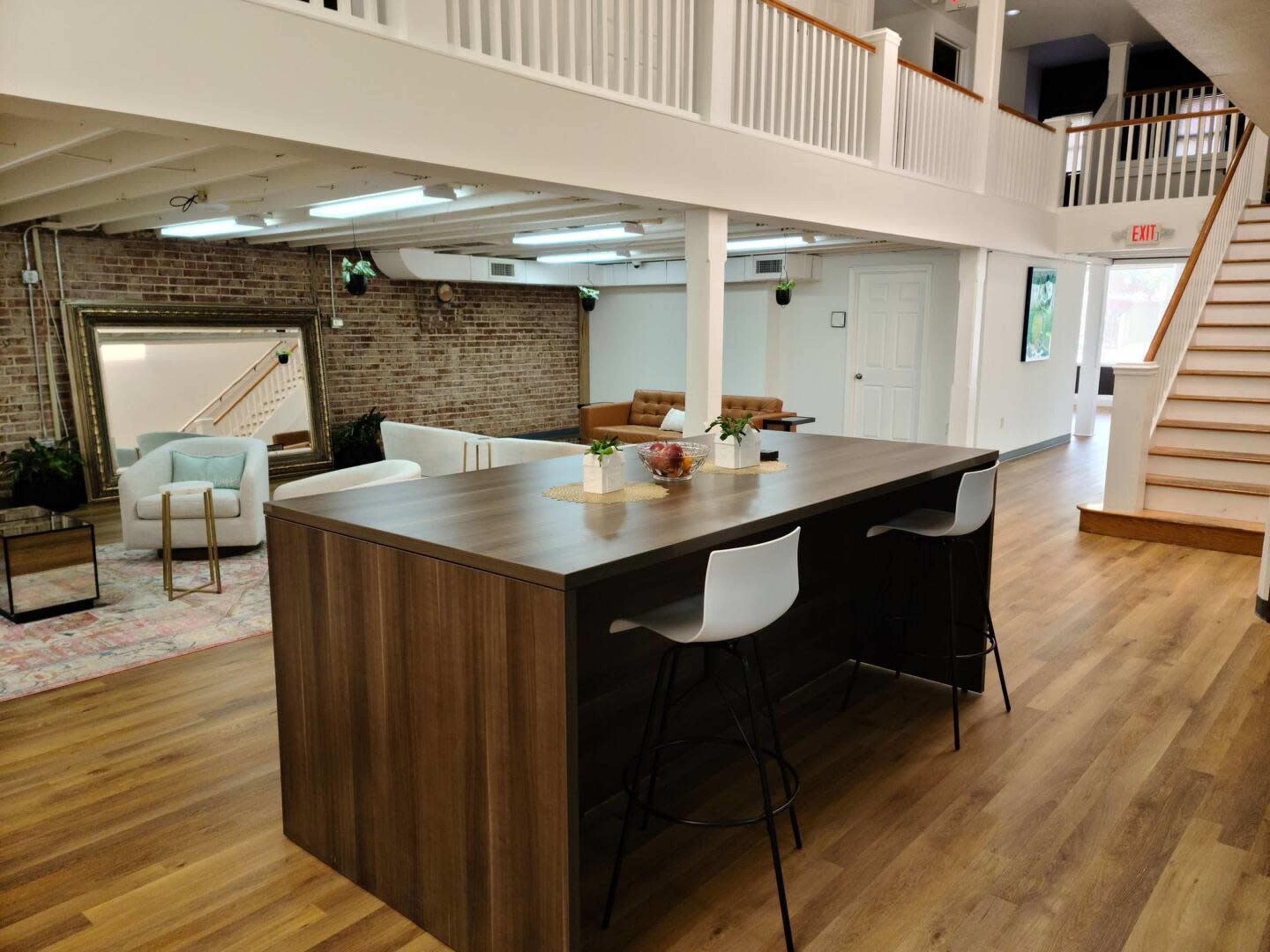 A spacious, open interior featuring a wooden island bar with two stools, a seating area with a couch and armchairs, and an exposed brick wall.