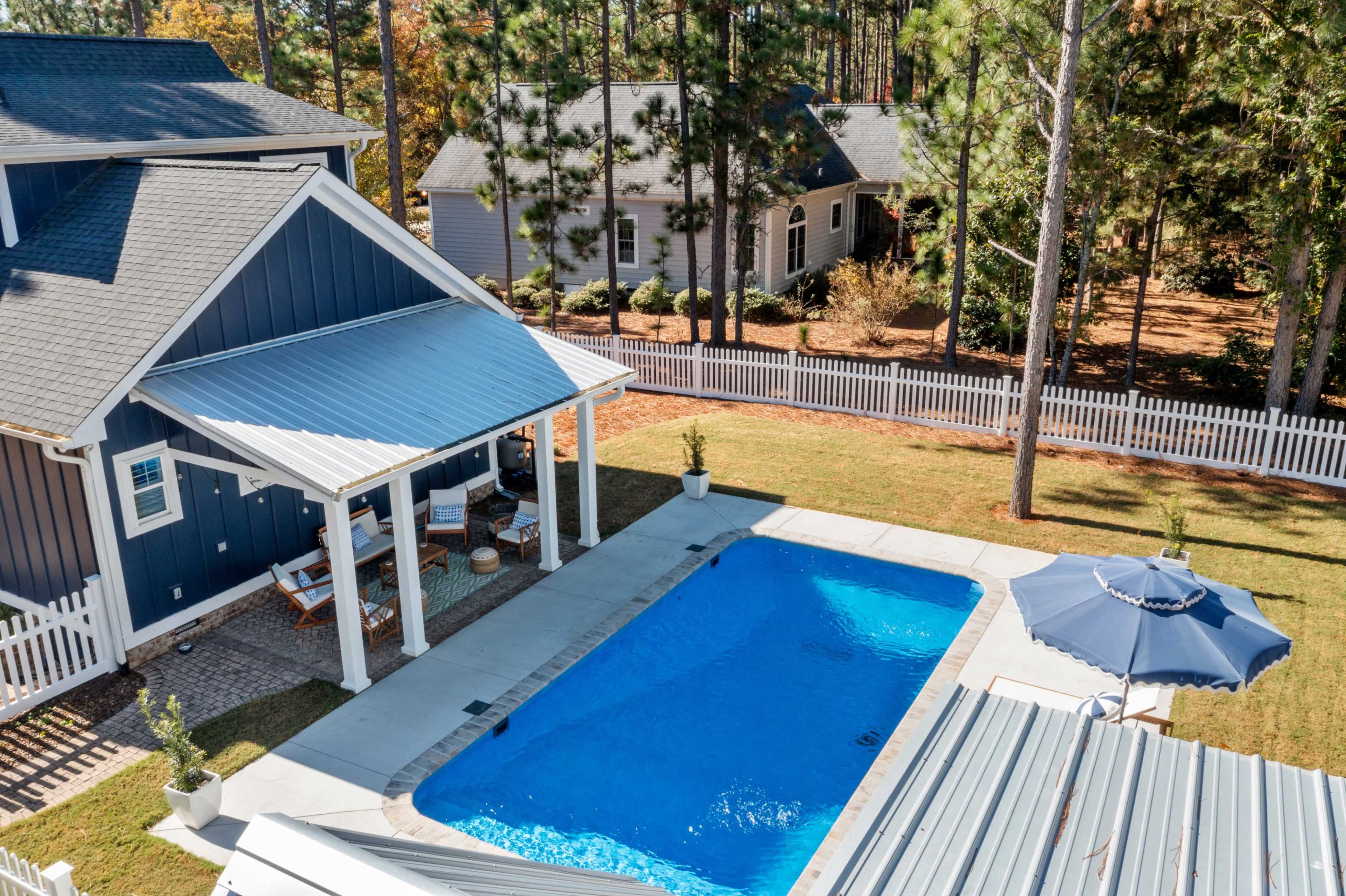 The image shows a backyard with a rectangular swimming pool surrounded by a patio, a gazebo, and several trees in the background.