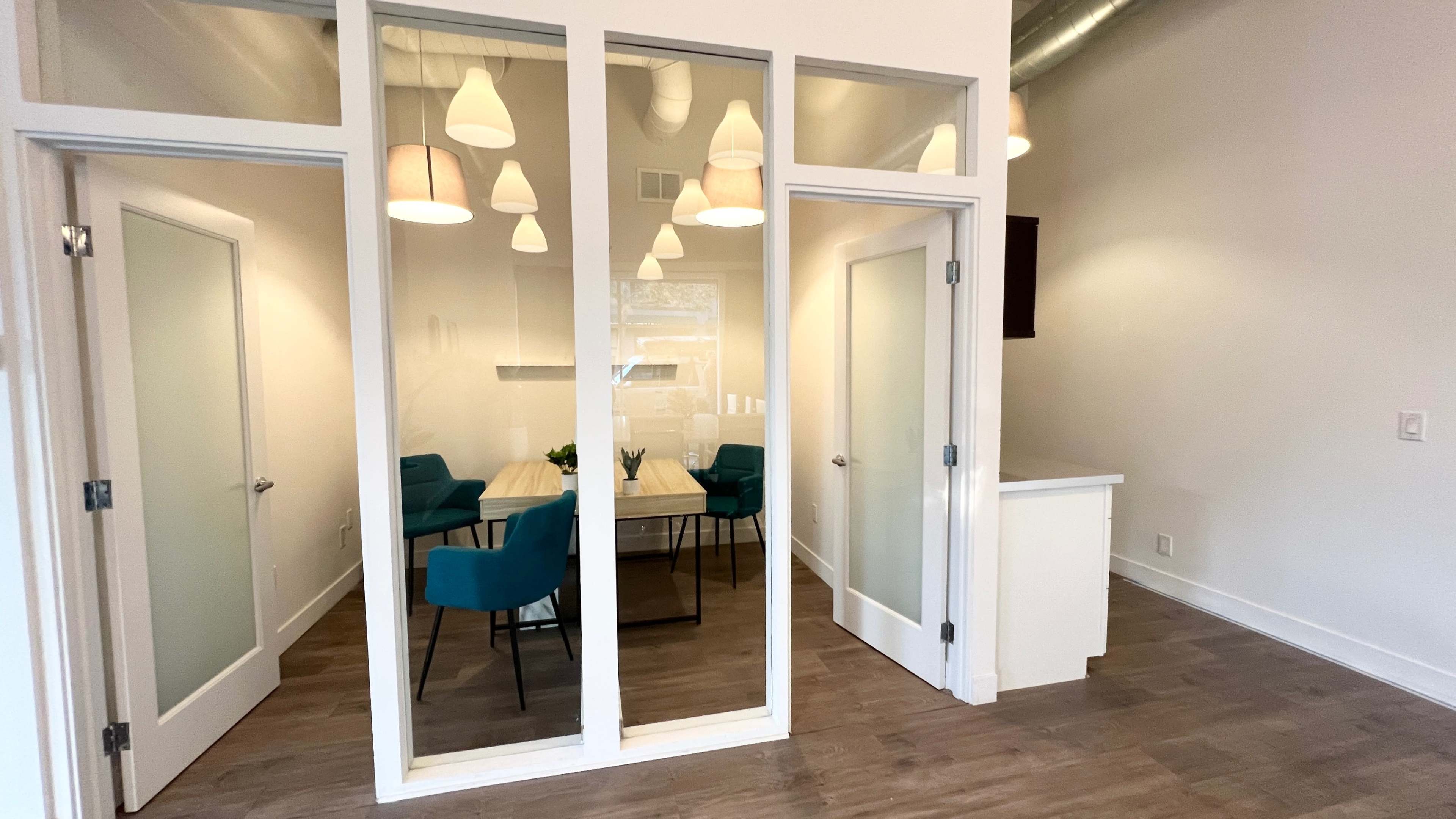 A modern office space with glass walls enclosing a conference room featuring a wooden table and chairs.