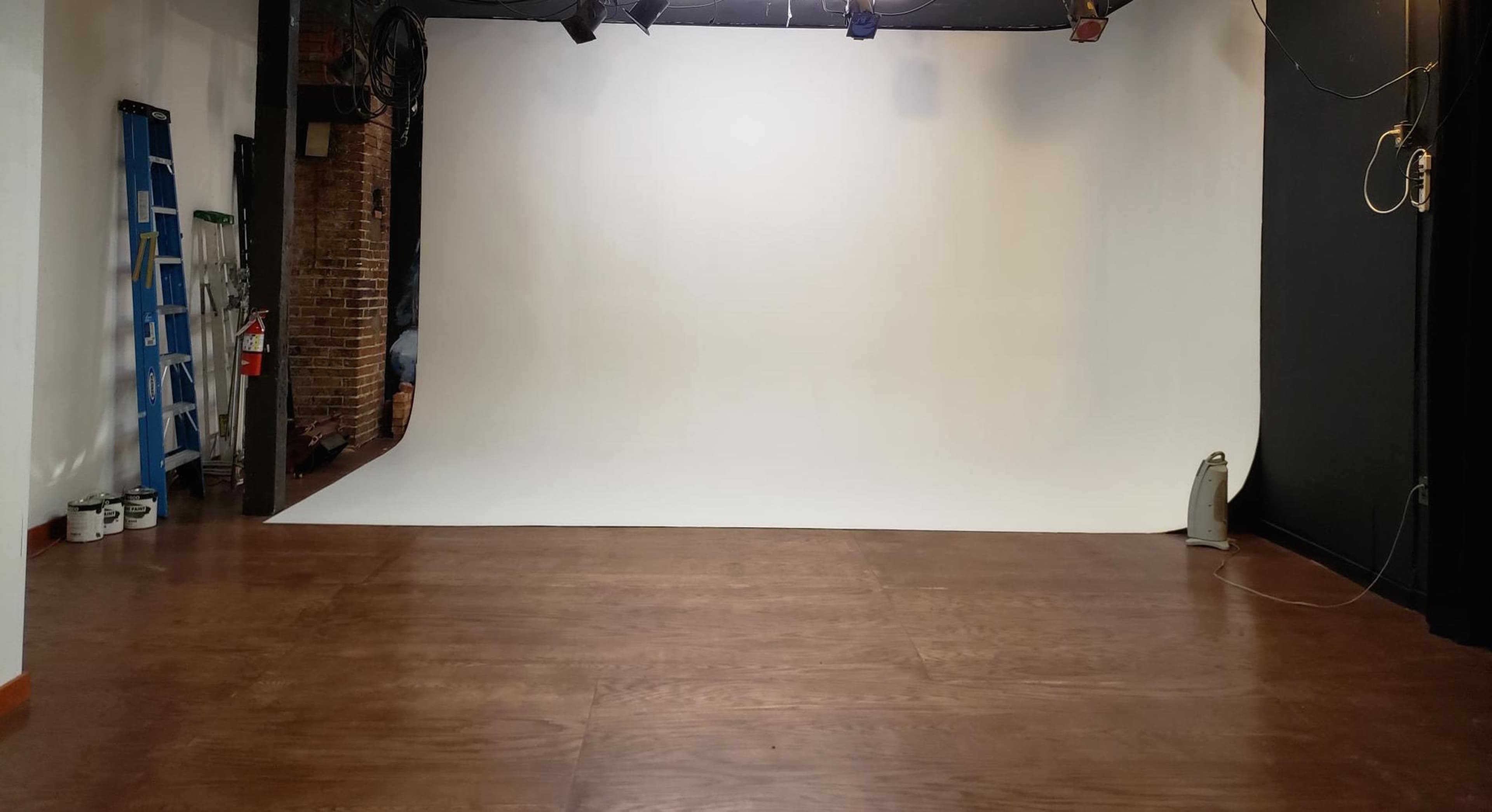 A spacious photography studio with a large white backdrop and wooden flooring.