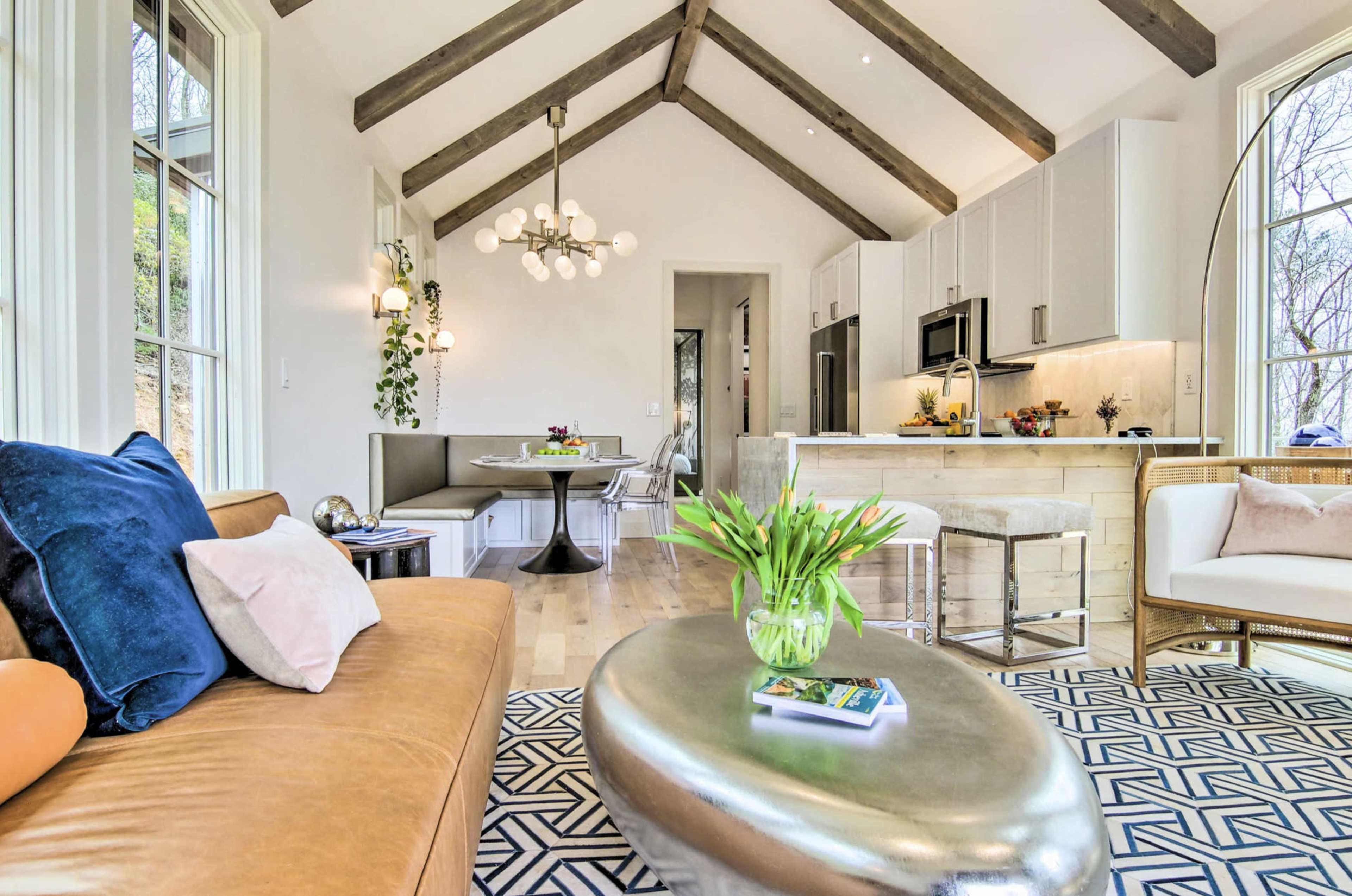 A modern living space featuring a brown leather sofa, a circular metallic coffee table, and a kitchenette with light cabinetry and a dining area.