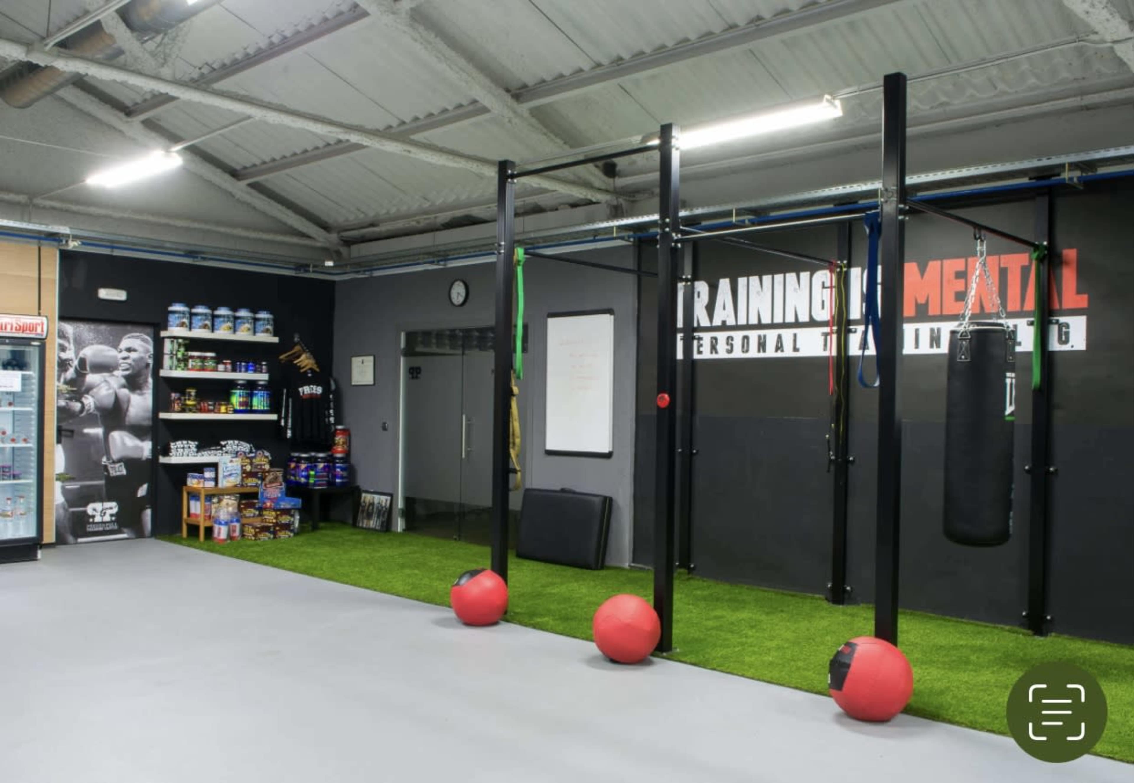 A modern gym interior with fitness equipment, including a punching bag and exercise balls, along with shelves displaying supplements.