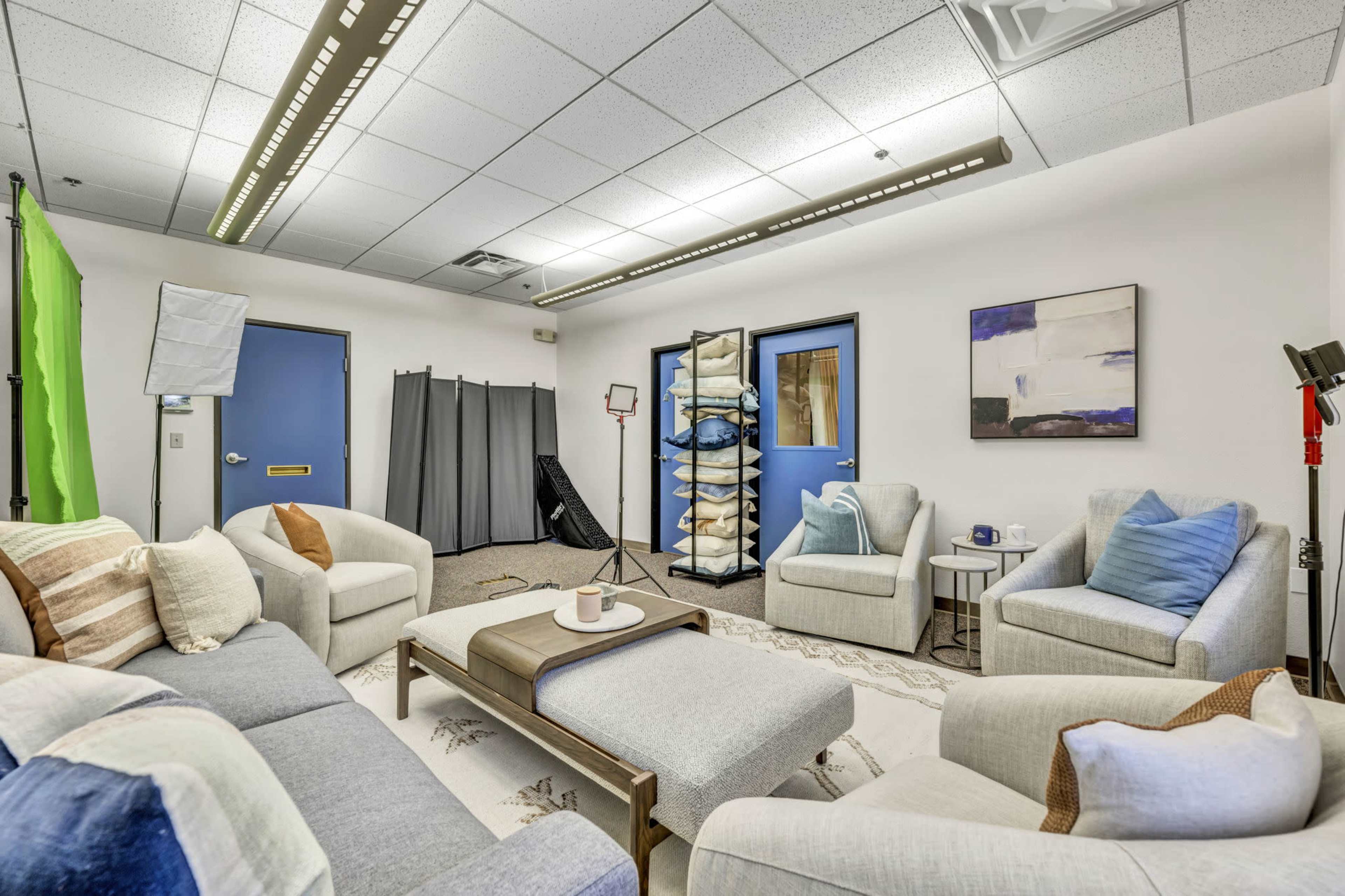 A modern, well-lit room featuring a seating area with light-colored sofas, a coffee table, and various props arranged against blue walls.
