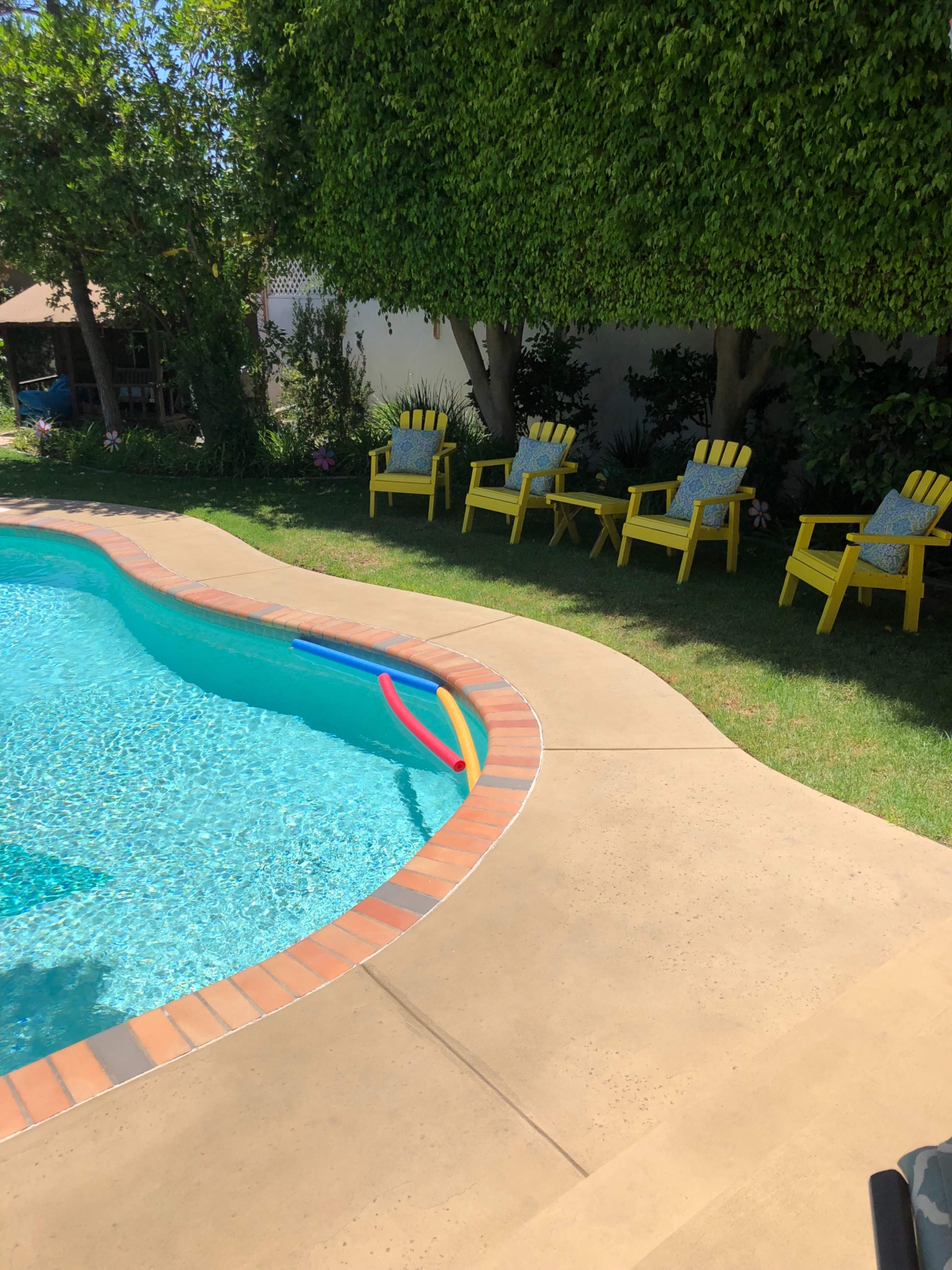 A swimming pool with colorful floats is surrounded by several yellow chairs on a concrete deck.