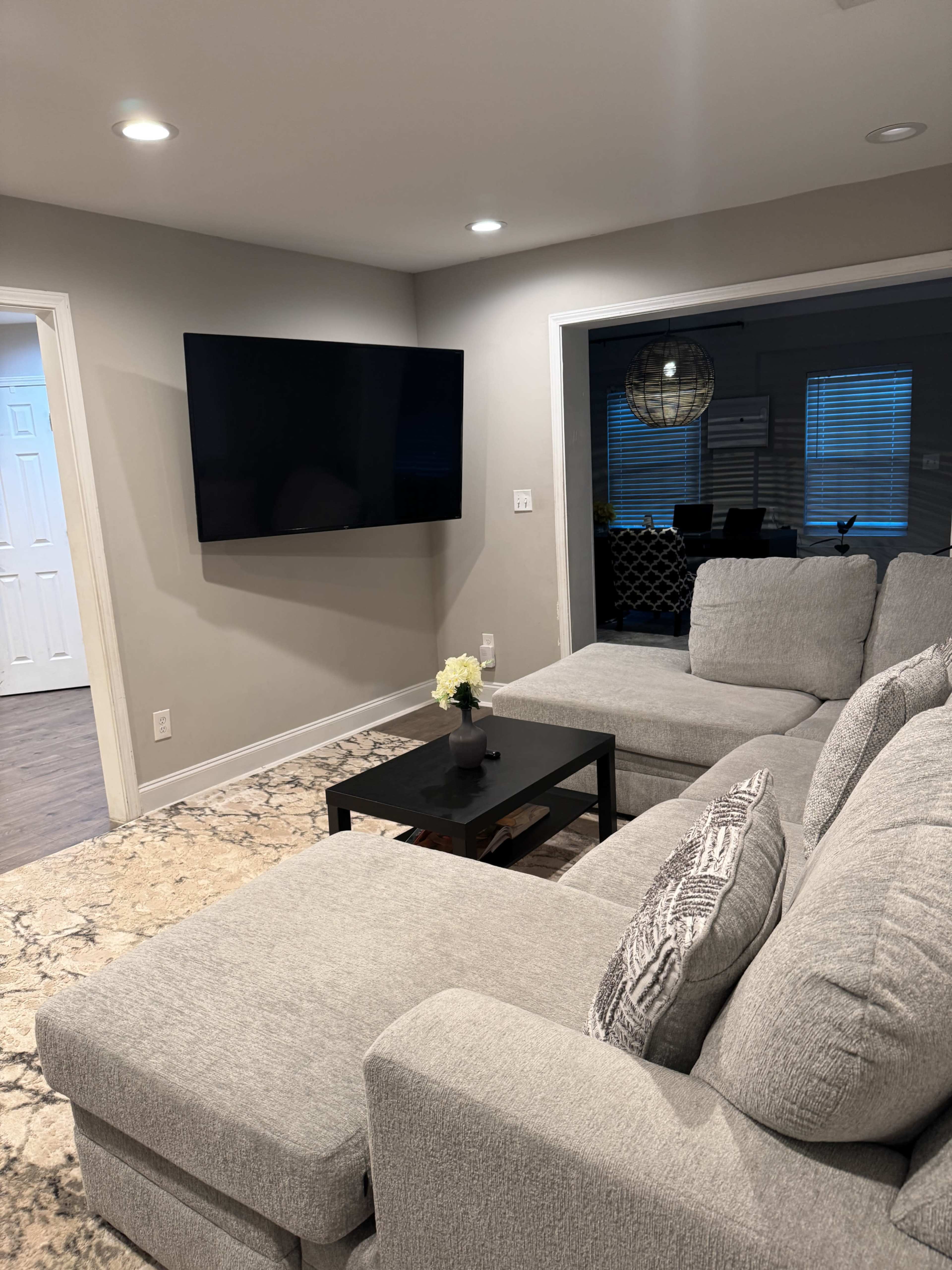 The image shows a modern living room featuring a large sectional sofa, a coffee table, and a wall-mounted television.
