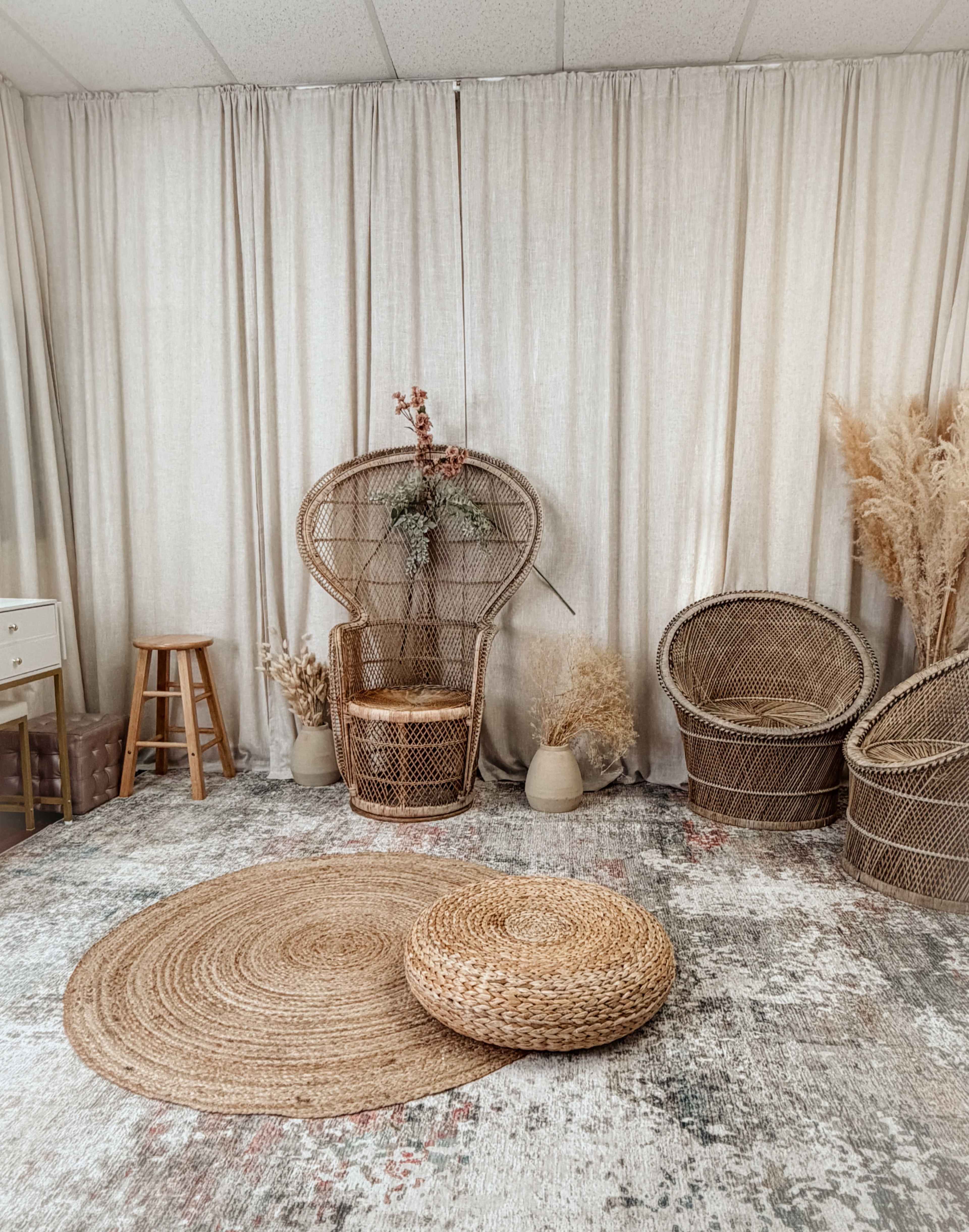 The image depicts a cozy room with natural elements, featuring woven furniture, a round rug, and decorative plants against a backdrop of light curtains.