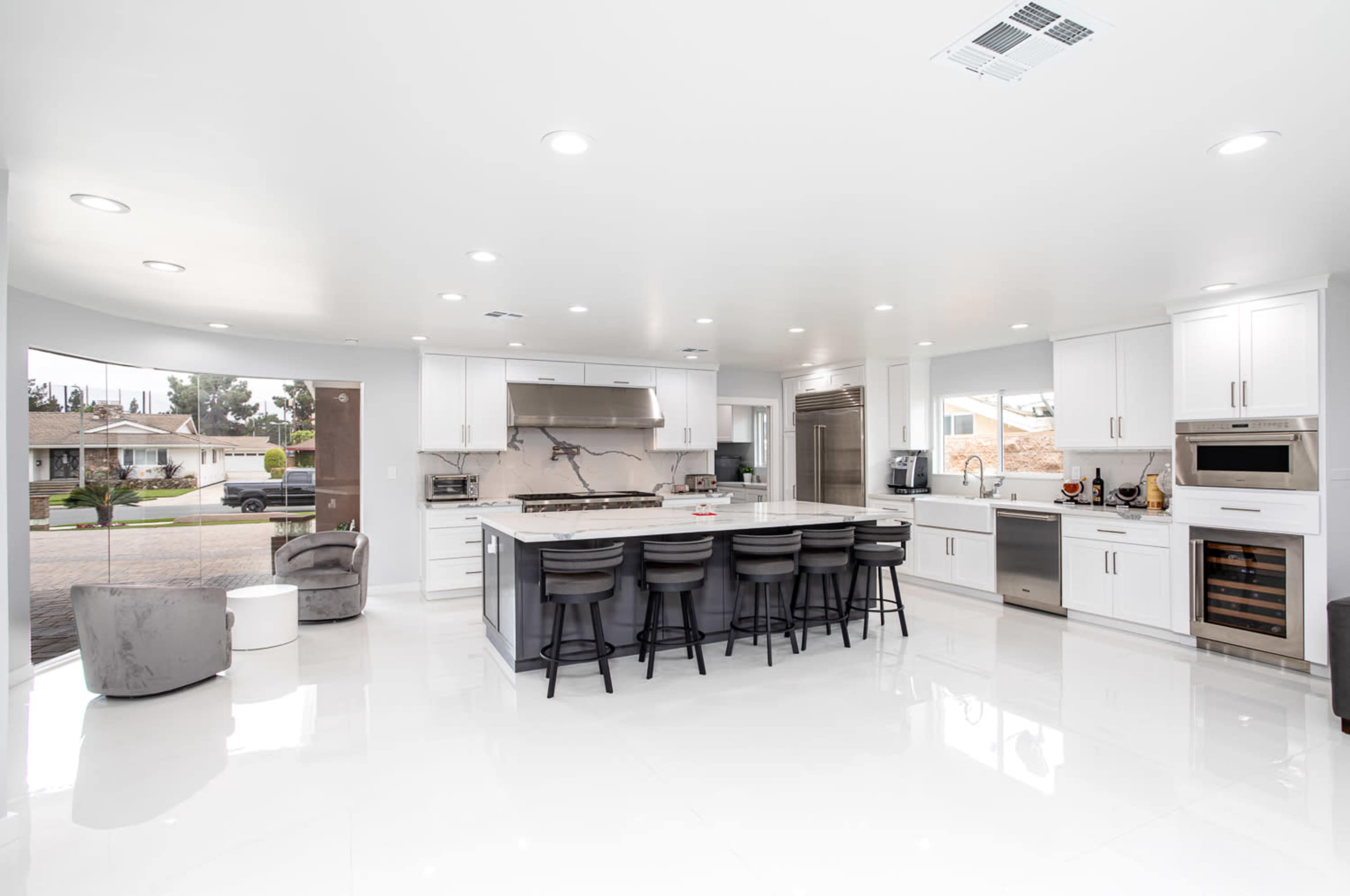 A modern kitchen features an island with bar seating, stainless steel appliances, and white cabinetry, illuminated by recessed lighting.