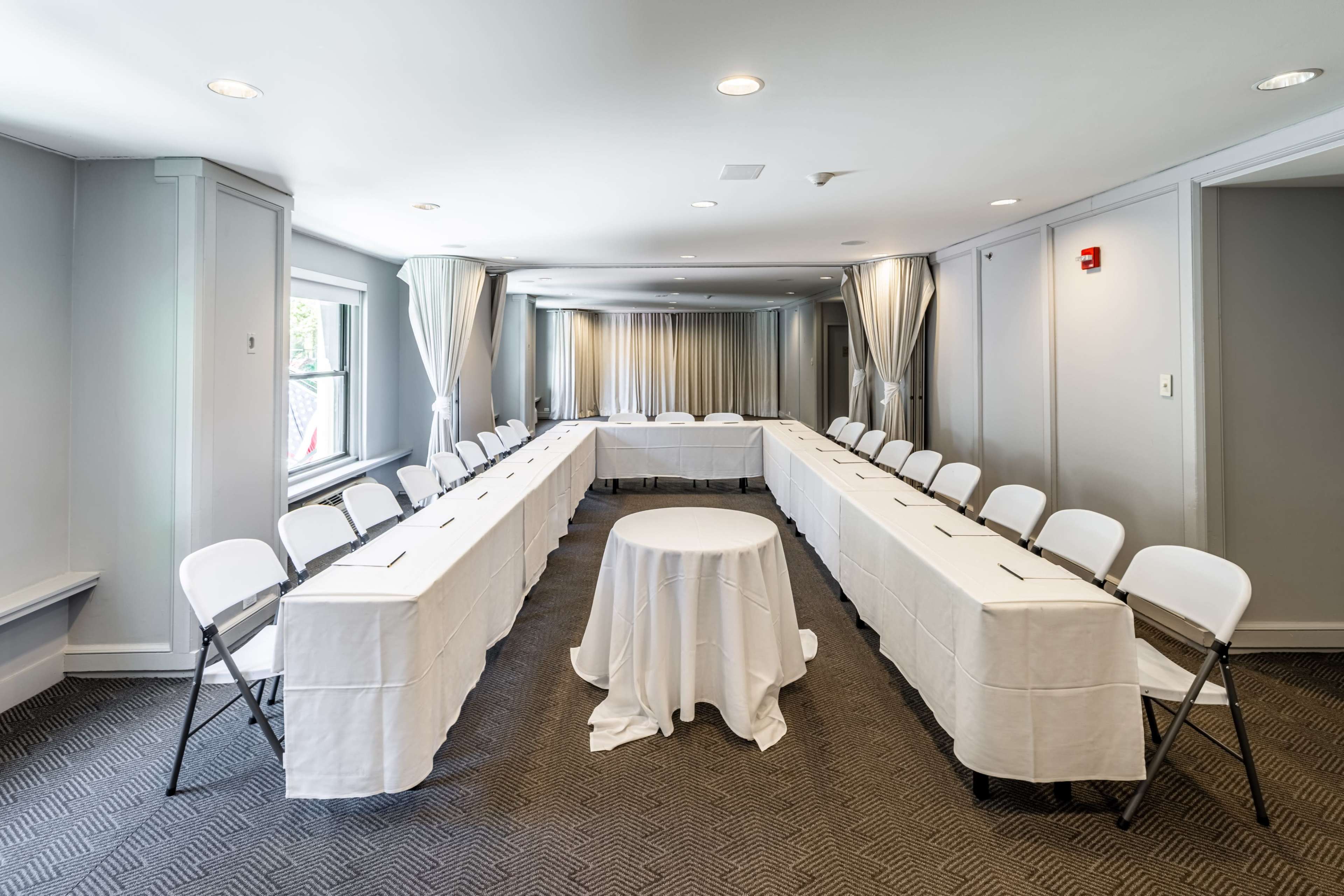 A conference room is arranged with two long tables set in a U-shape, surrounded by white folding chairs, with a round table at the center.