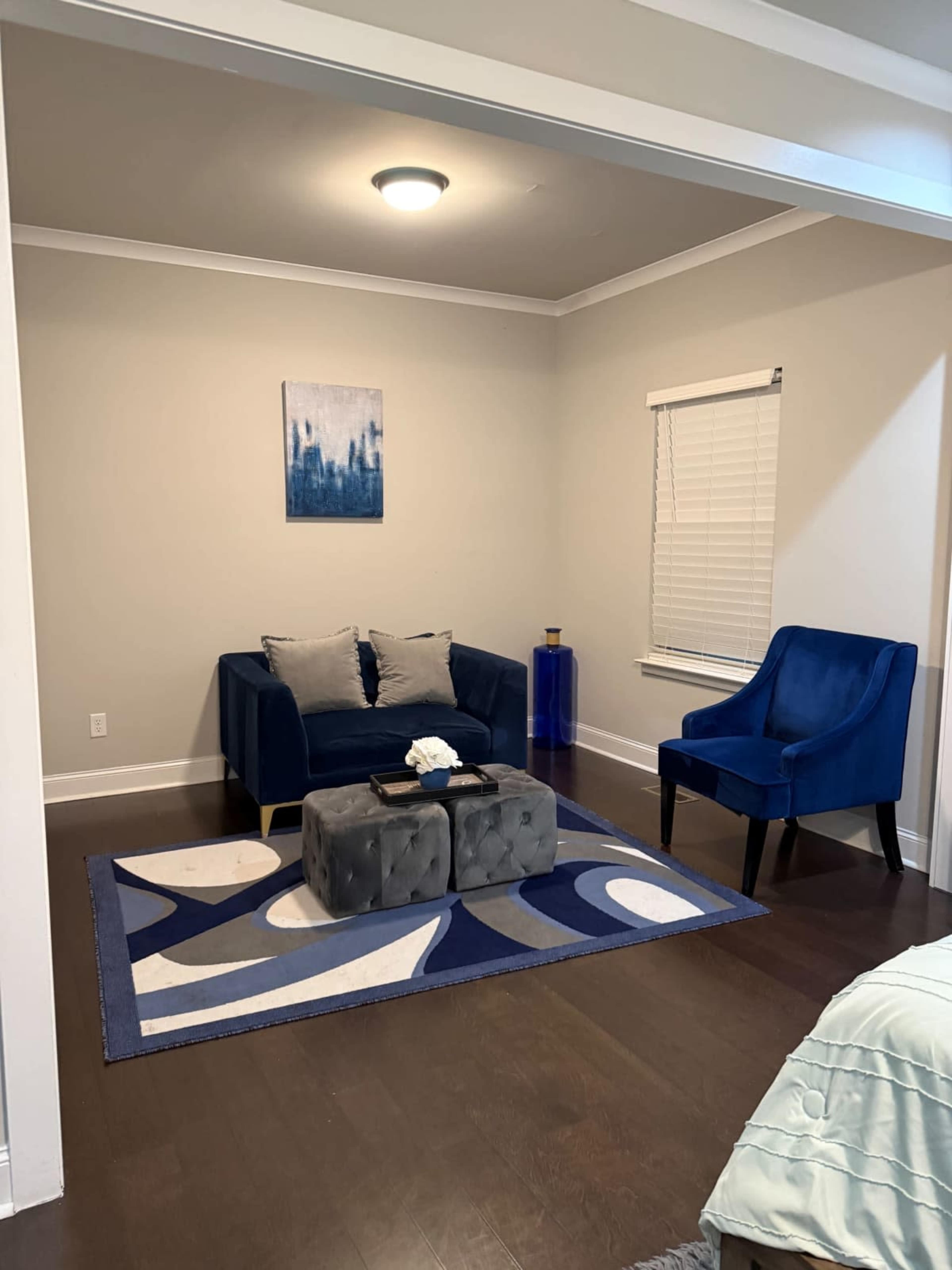 The image shows a modern living room featuring a blue couch, a matching chair, a rug with geometric patterns, and a small coffee table.