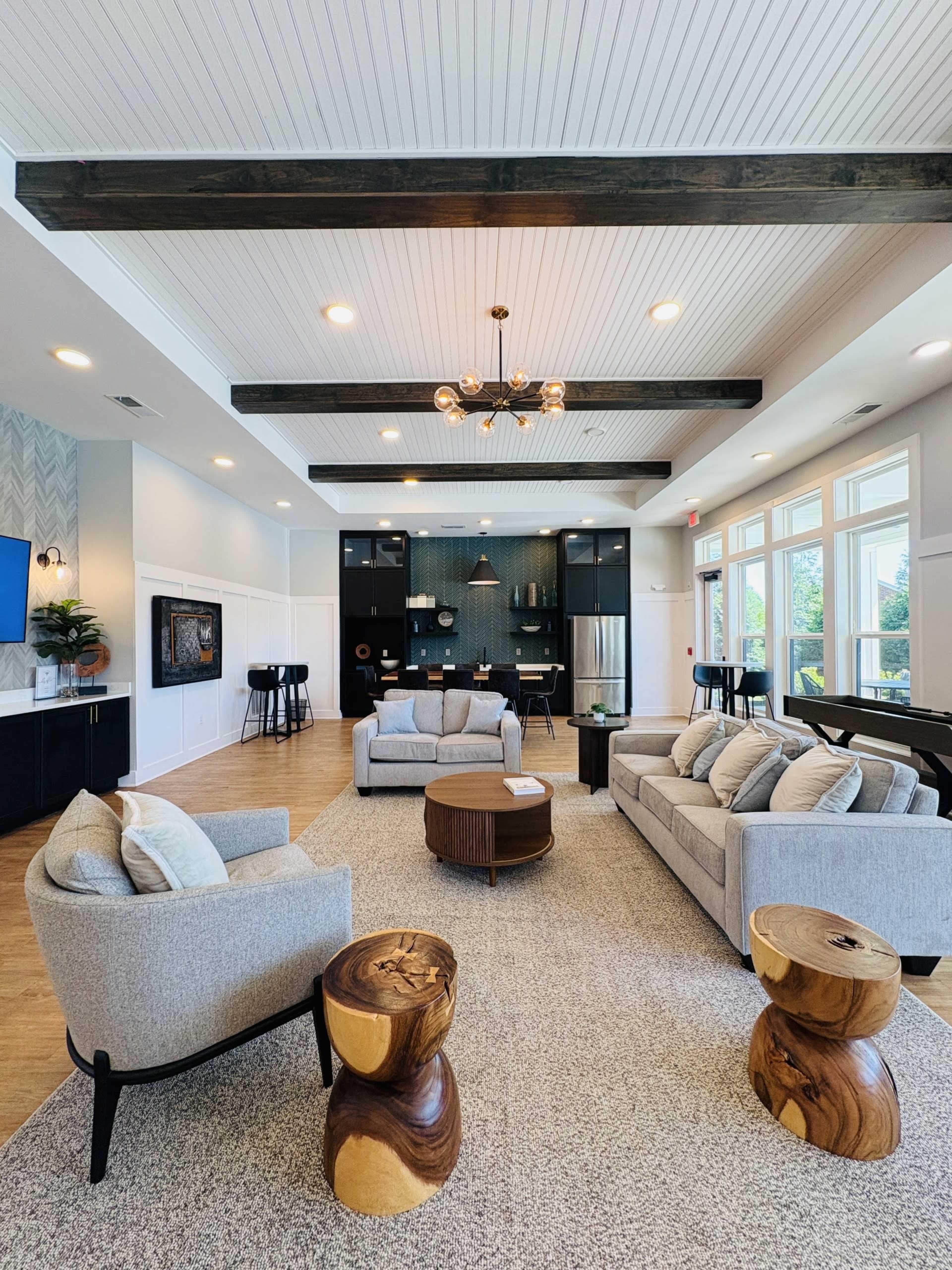 The image shows a modern living area with two gray sofas, a wooden coffee table, and two unique wooden side tables, all set beneath a coffered ceiling with exposed beams.