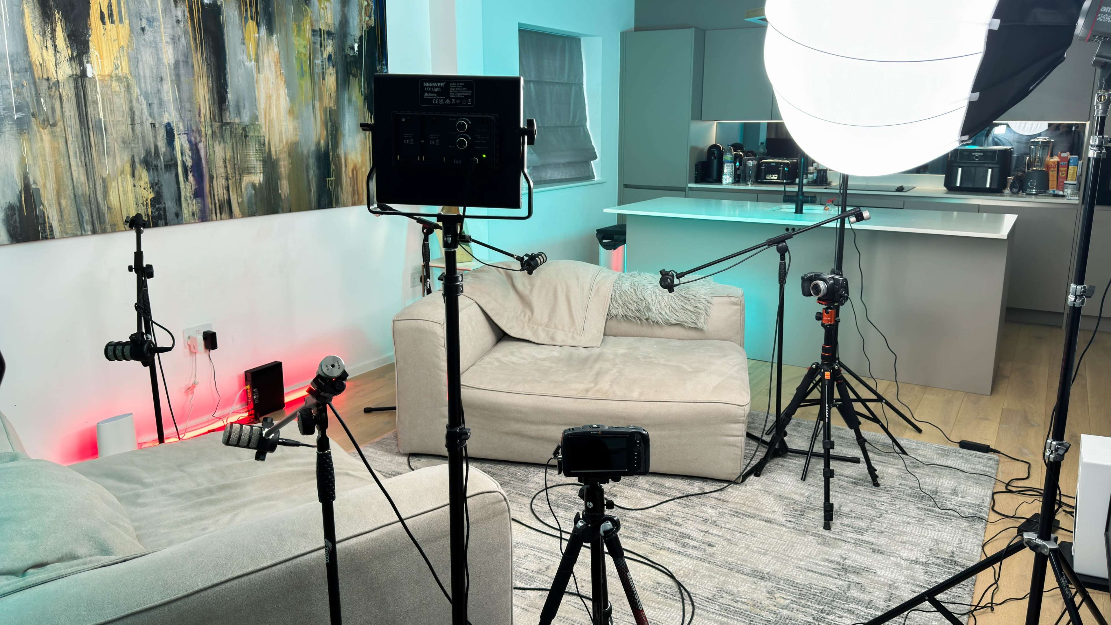 A modern room set up for a video shoot, featuring softbox lights, multiple tripods, and a light-colored couch.