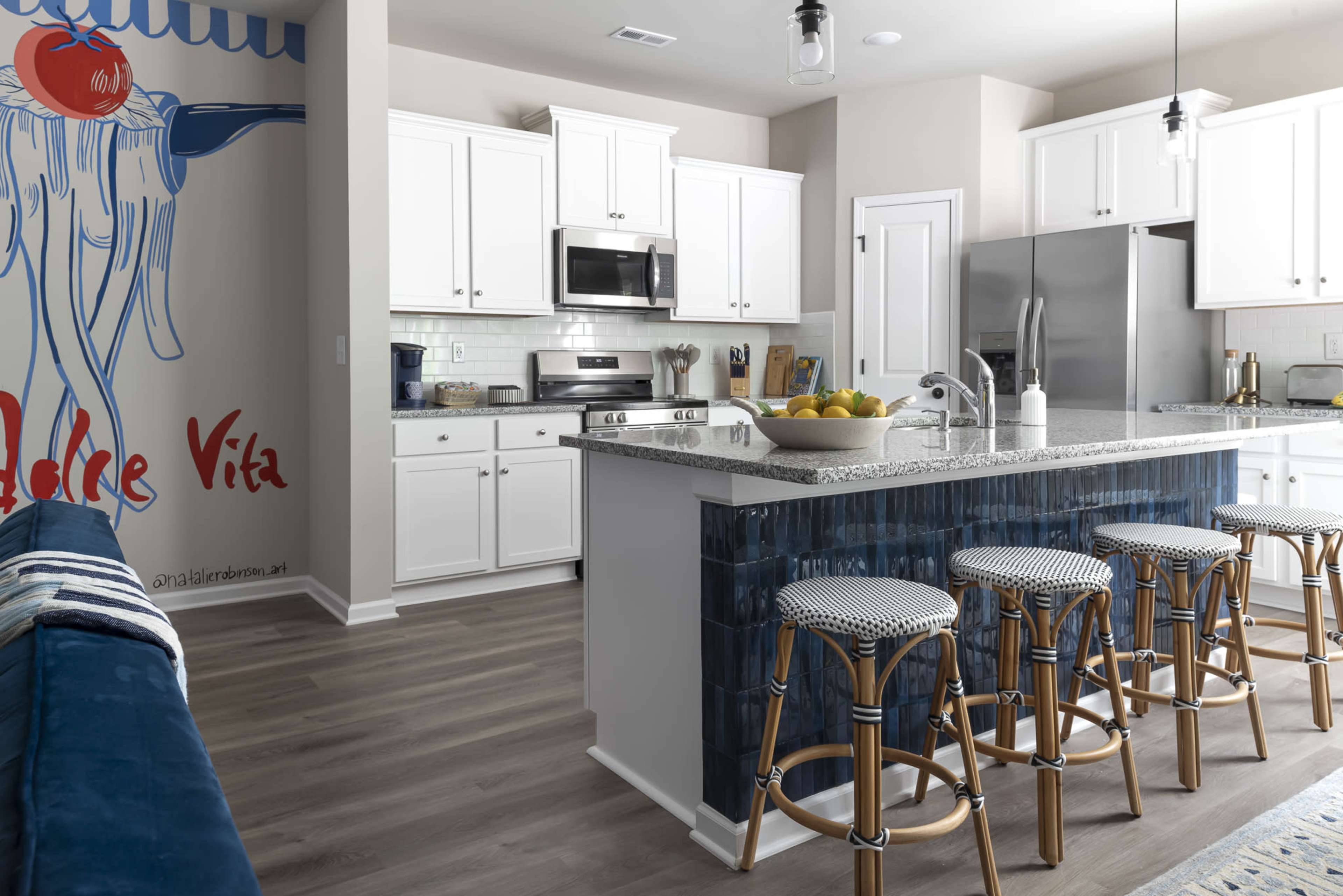 A modern kitchen features white cabinetry, stainless steel appliances, a large island with bar stools, and a mural on the wall.