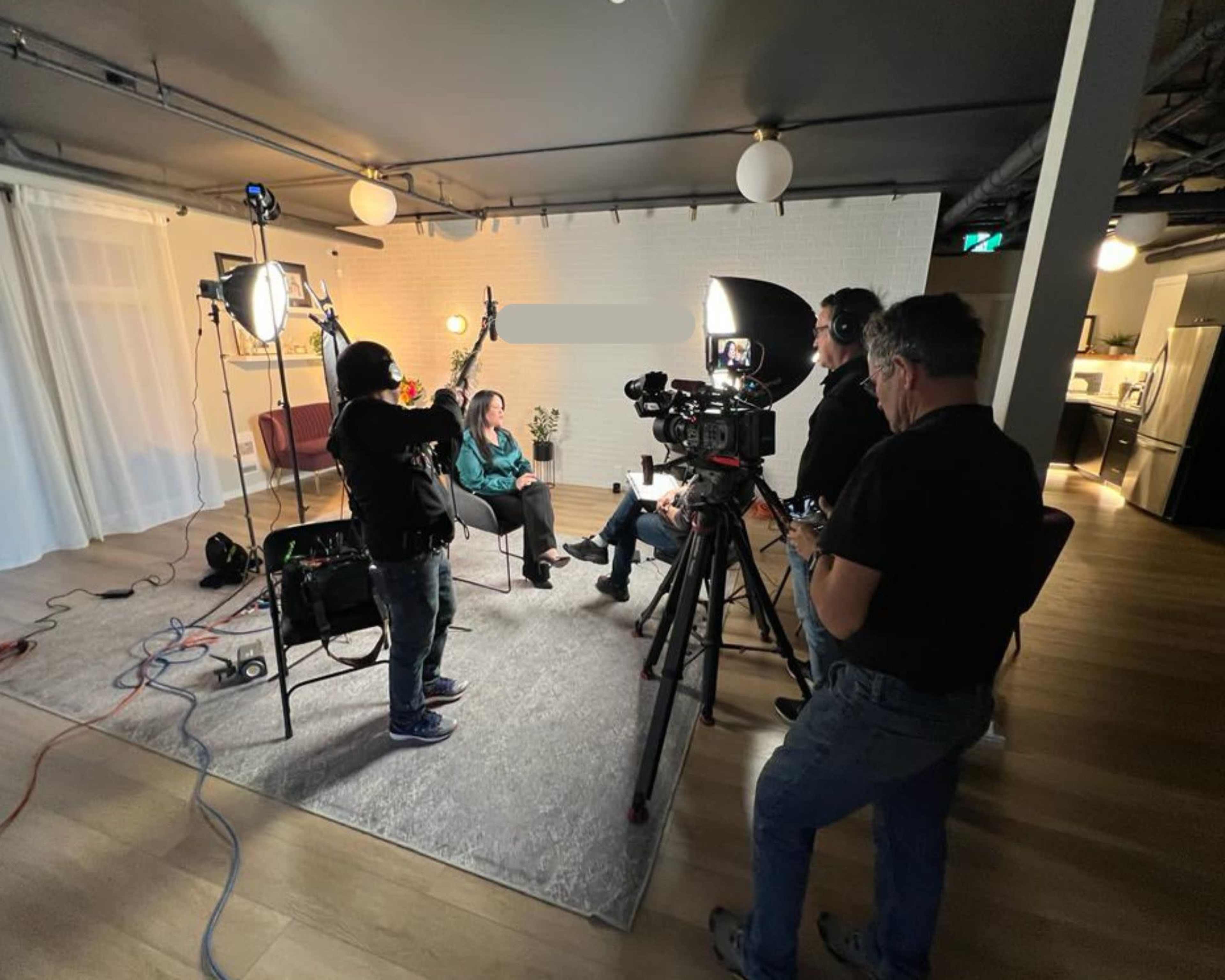A film crew sets up equipment around a woman being interviewed in a modern indoor space.