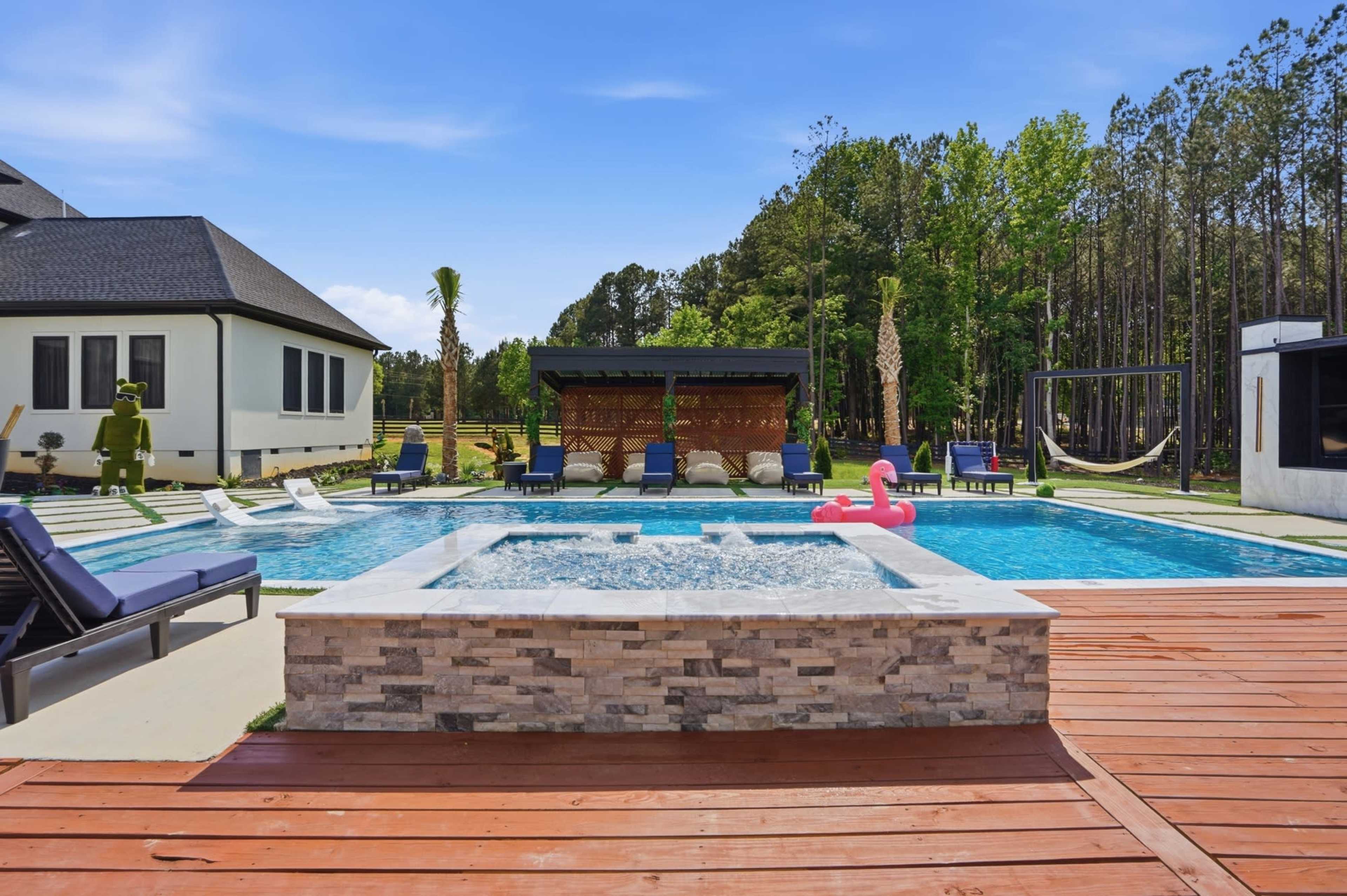 The image shows a landscaped backyard featuring a swimming pool with a spa, surrounded by lounge chairs and trees in the background.