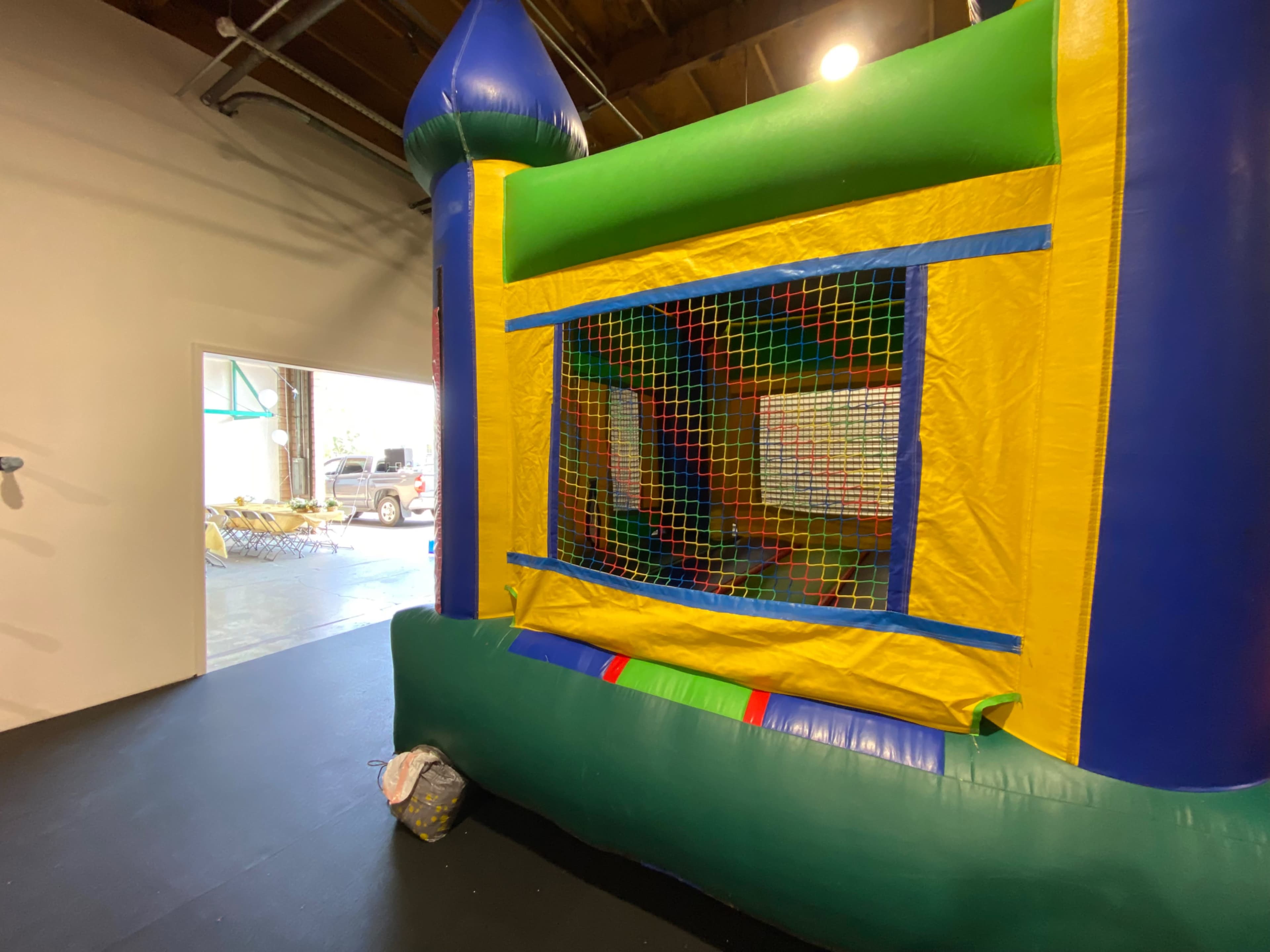 A colorful bounce house with a netted opening is positioned in an indoor space next to an open door.
