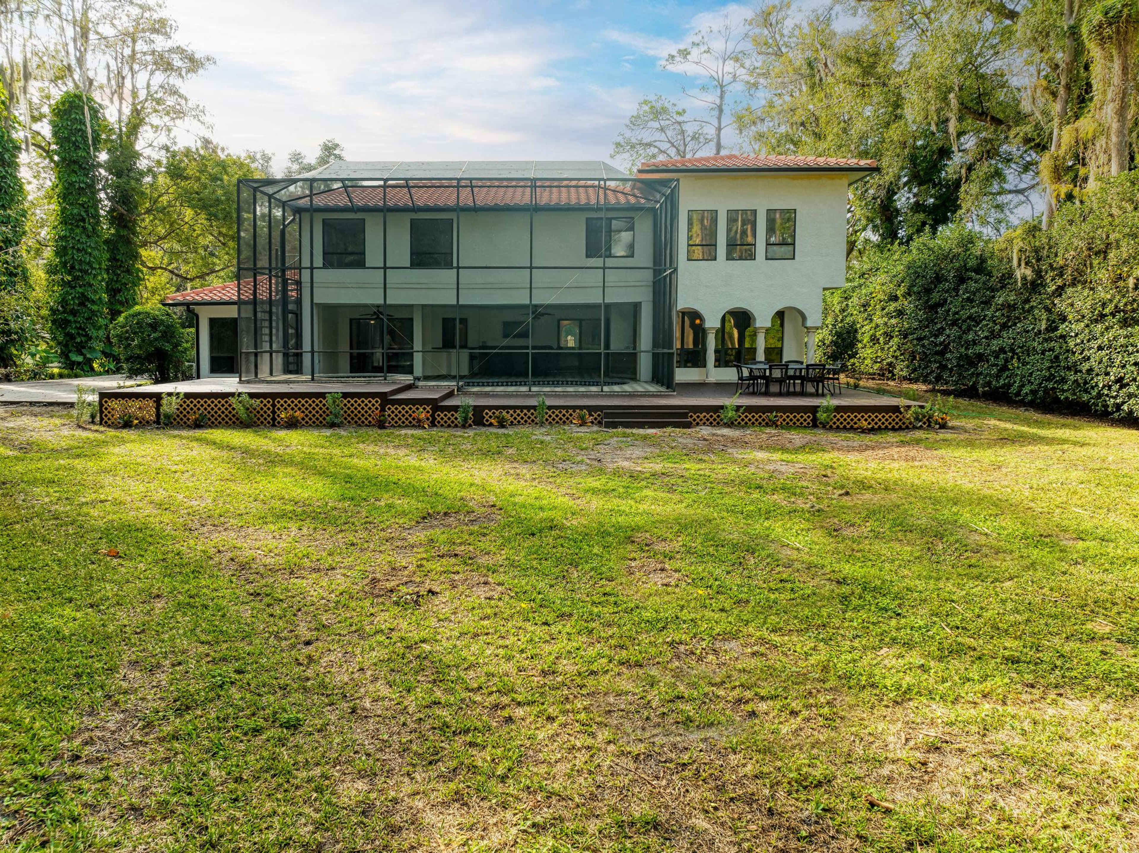 A two-story house with a large screened patio is surrounded by a grassy yard and trees.