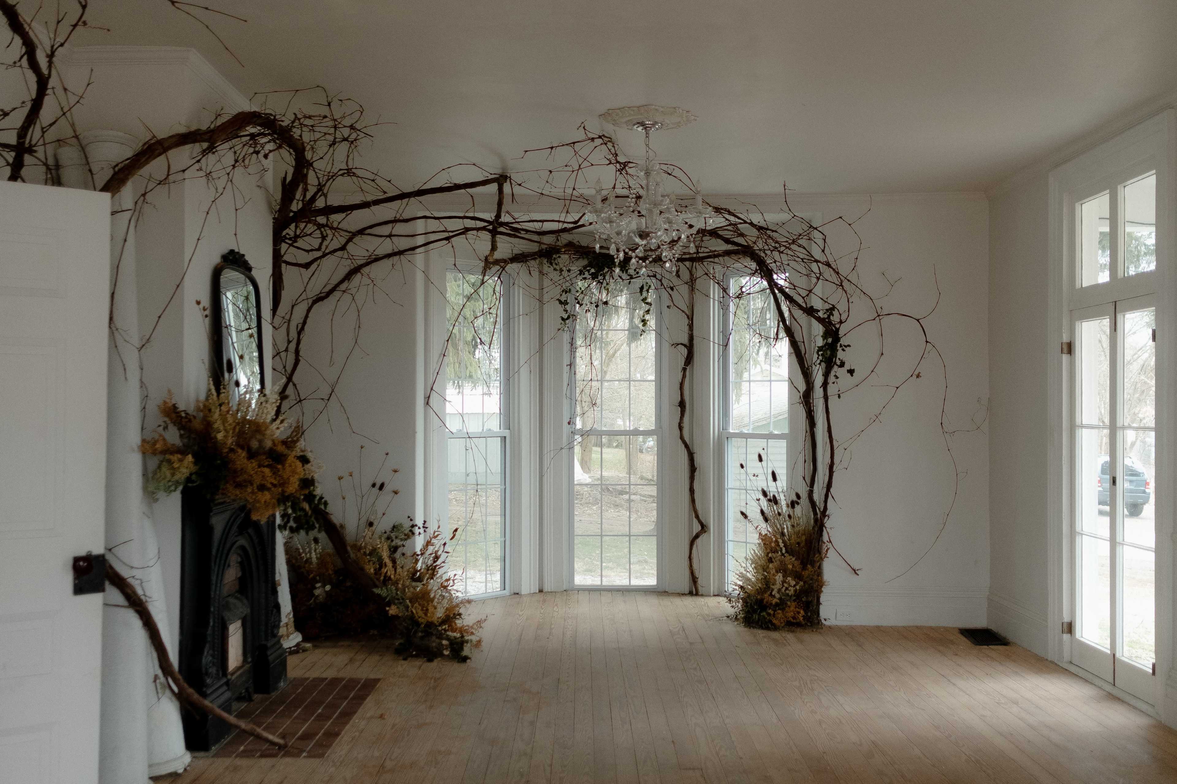 The room features large windows, a chandelier, and natural elements like branches and dried flowers decorating the walls and floor.