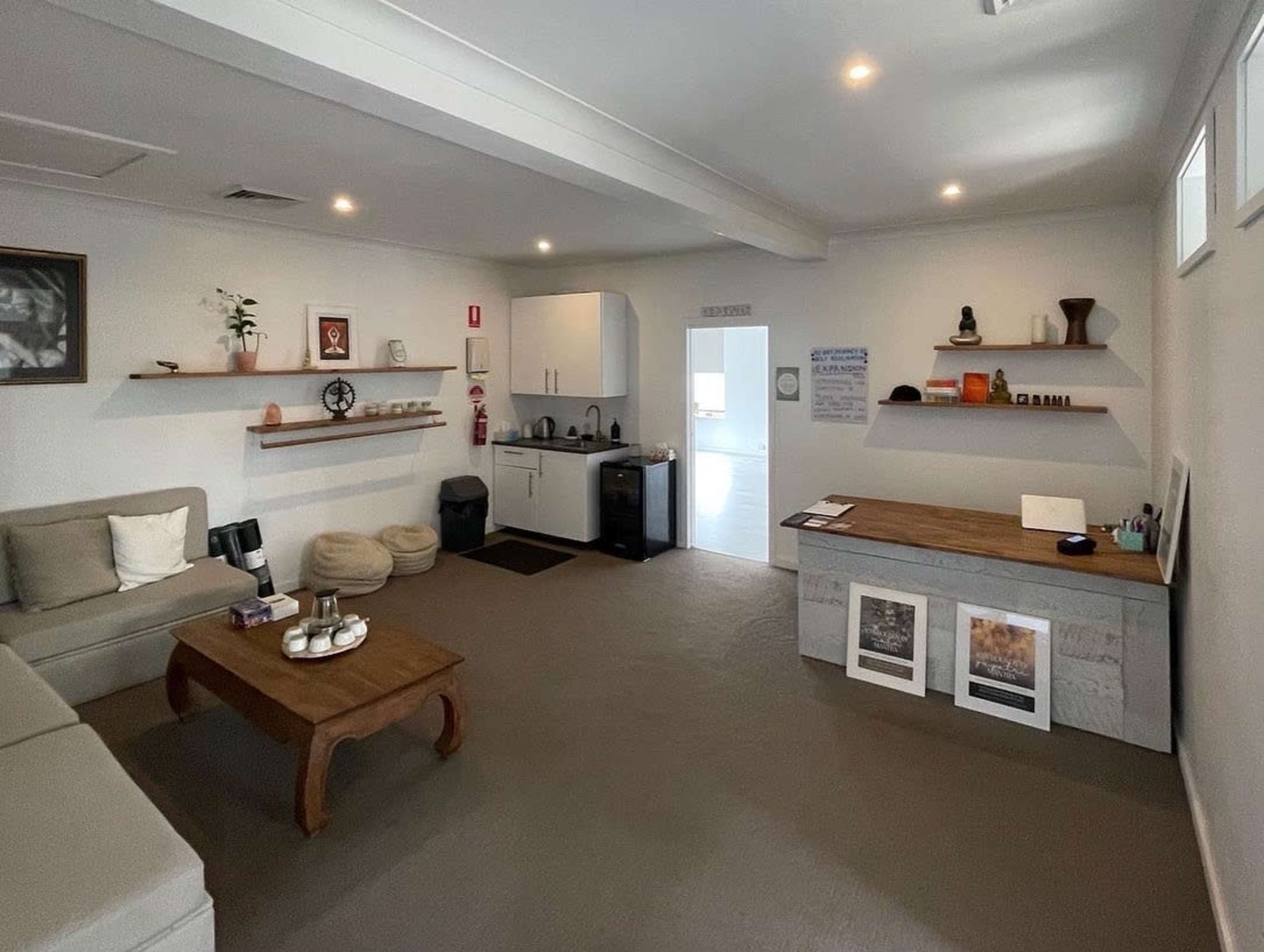A modern, minimalist interior of a room featuring a sofa, a coffee table, a kitchenette, and shelves with decorative items.